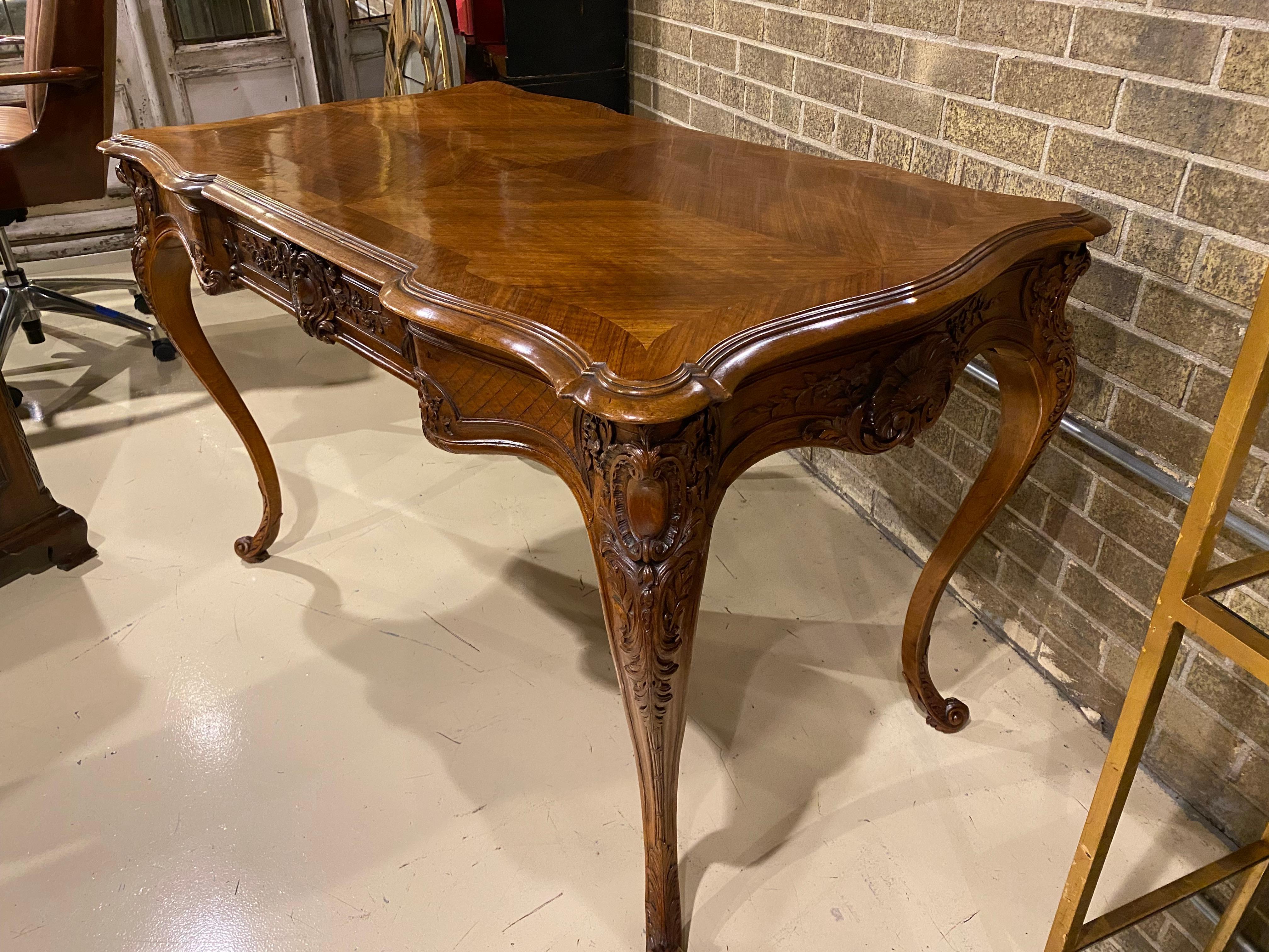A beautifully proportioned 19th century French style writing table or desk, crafted in walnut with a lovely pattern walnut top with a walnut edge band. The carving is nicely detailed around the apron of the table and conceals one drawer that has a