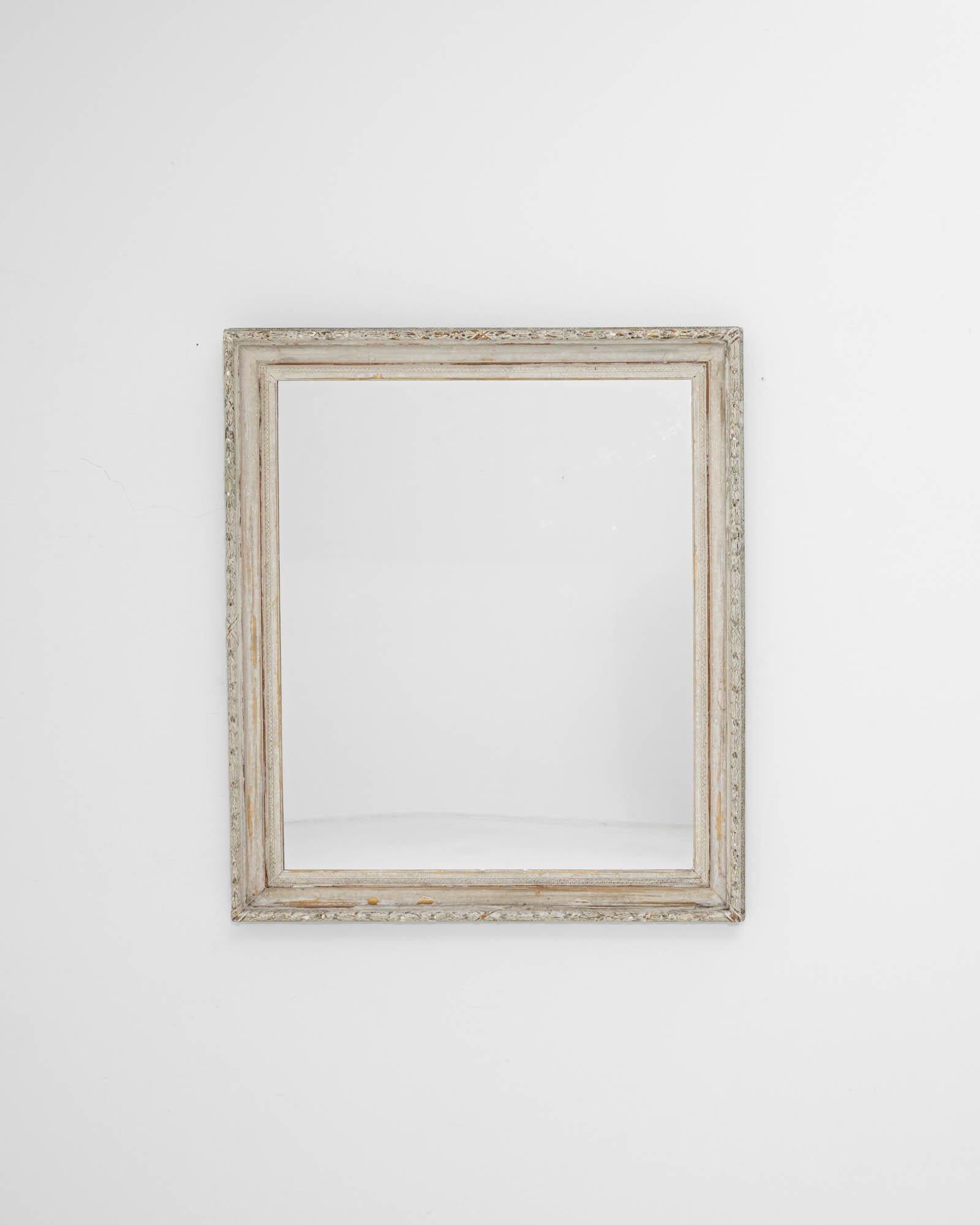 A wooden mirror created in 19th century France. The time-touched frame, adorned with captivating detail, leads the eye around its edges. The white patina has enhanced with age, drawing one in for a closer inspection. Profiled edges were sculpted