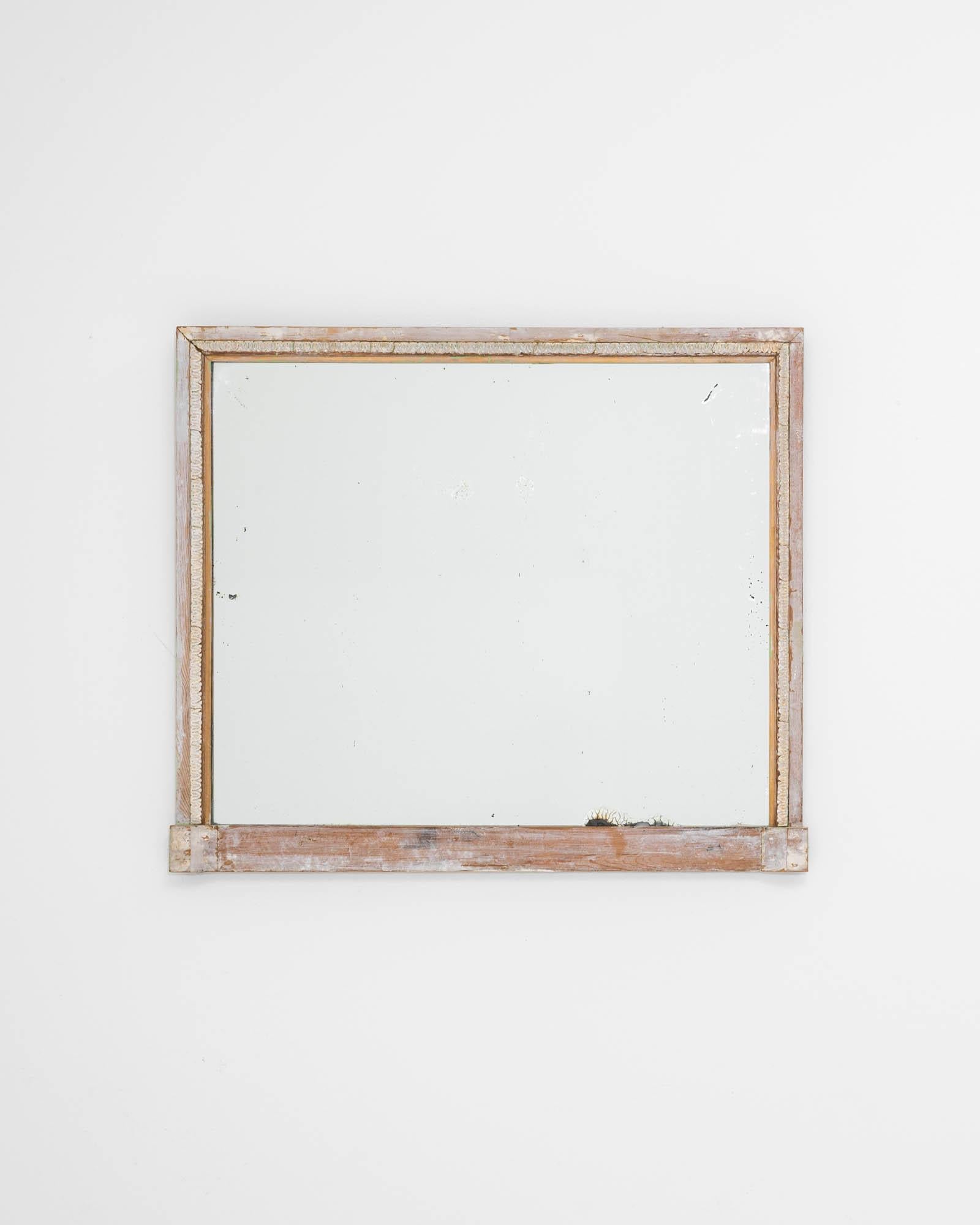 A wooden mirror created in 19th century France. Composed with an upright shape, a laurel of ornament crowns the top and sides of this timeless find. The white patina has been enhanced by time, drawing one in for a closer inspection. Classical motifs
