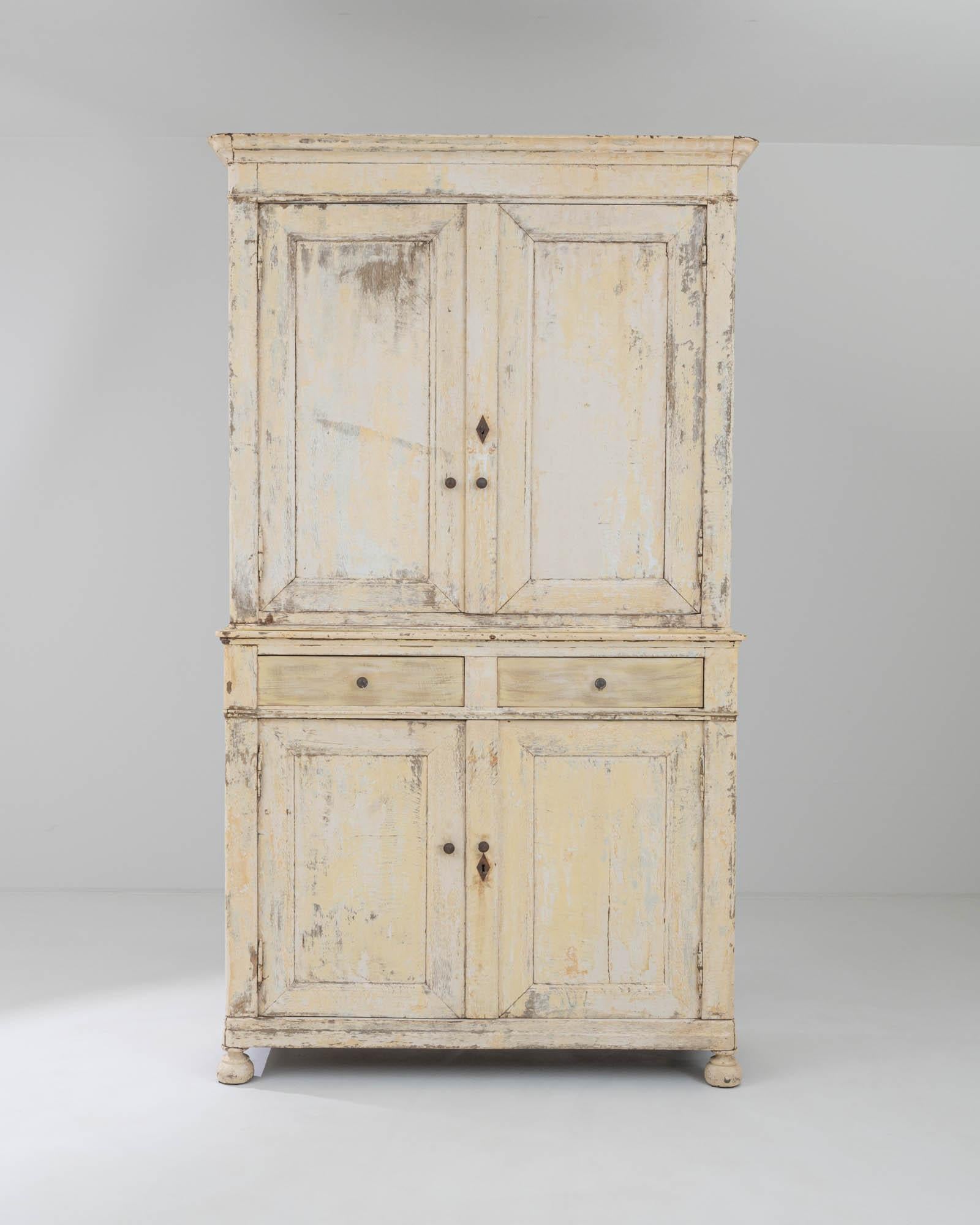 Sturdily resting on its carved bun feet, this antique wooden cabinet was made in 19th-century France. Its deux corps structure is gracefully divided by a set of drawers, creating a distinction between the spacious upper compartment with panel doors