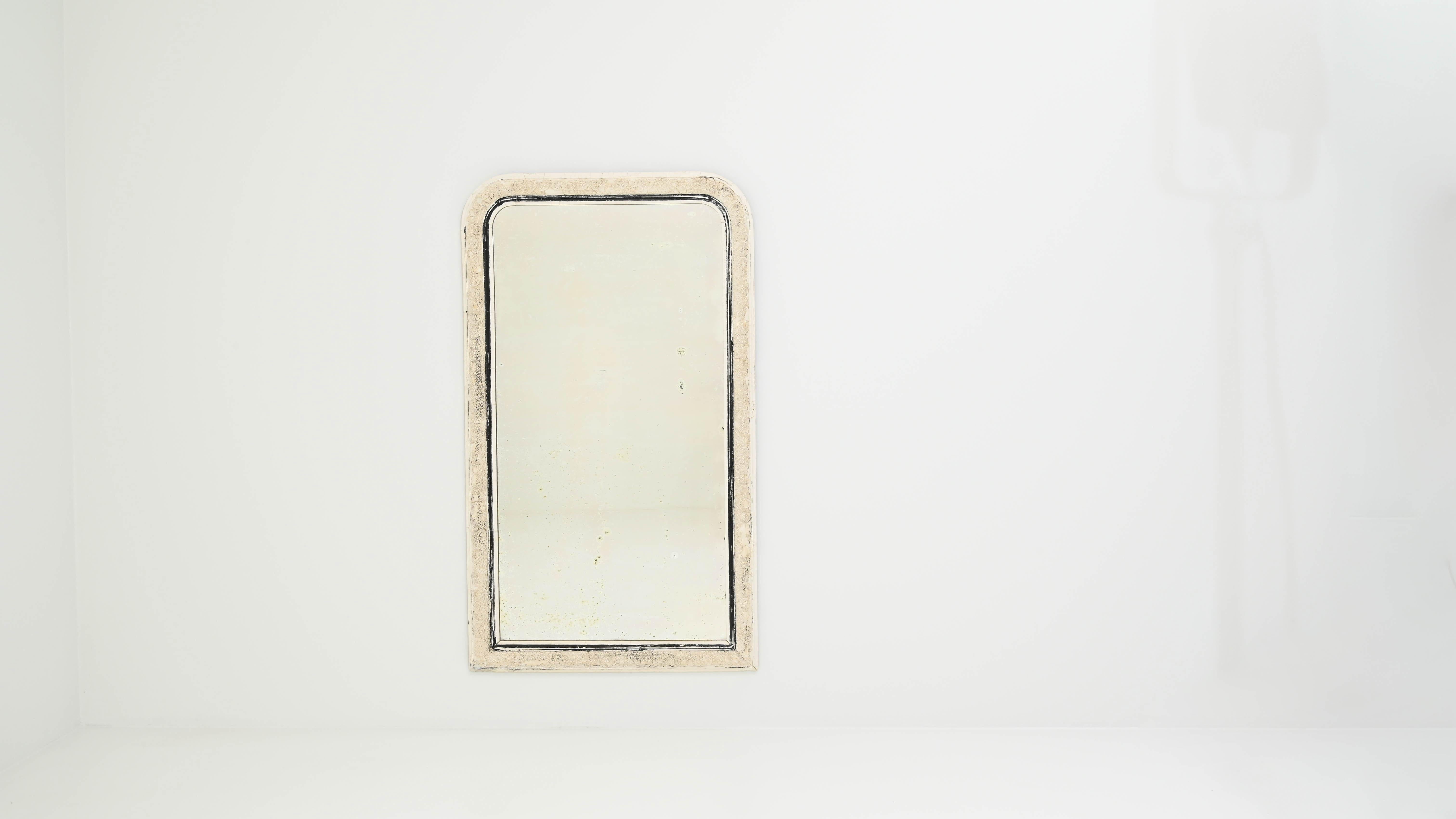 The delicate white patina of this 19th-century French mirror complements the softly-rounded upper corners, enhancing the graceful appeal of meticulous foliate patterns carved on the frame. The angular bottom corners create a captivating contrast,