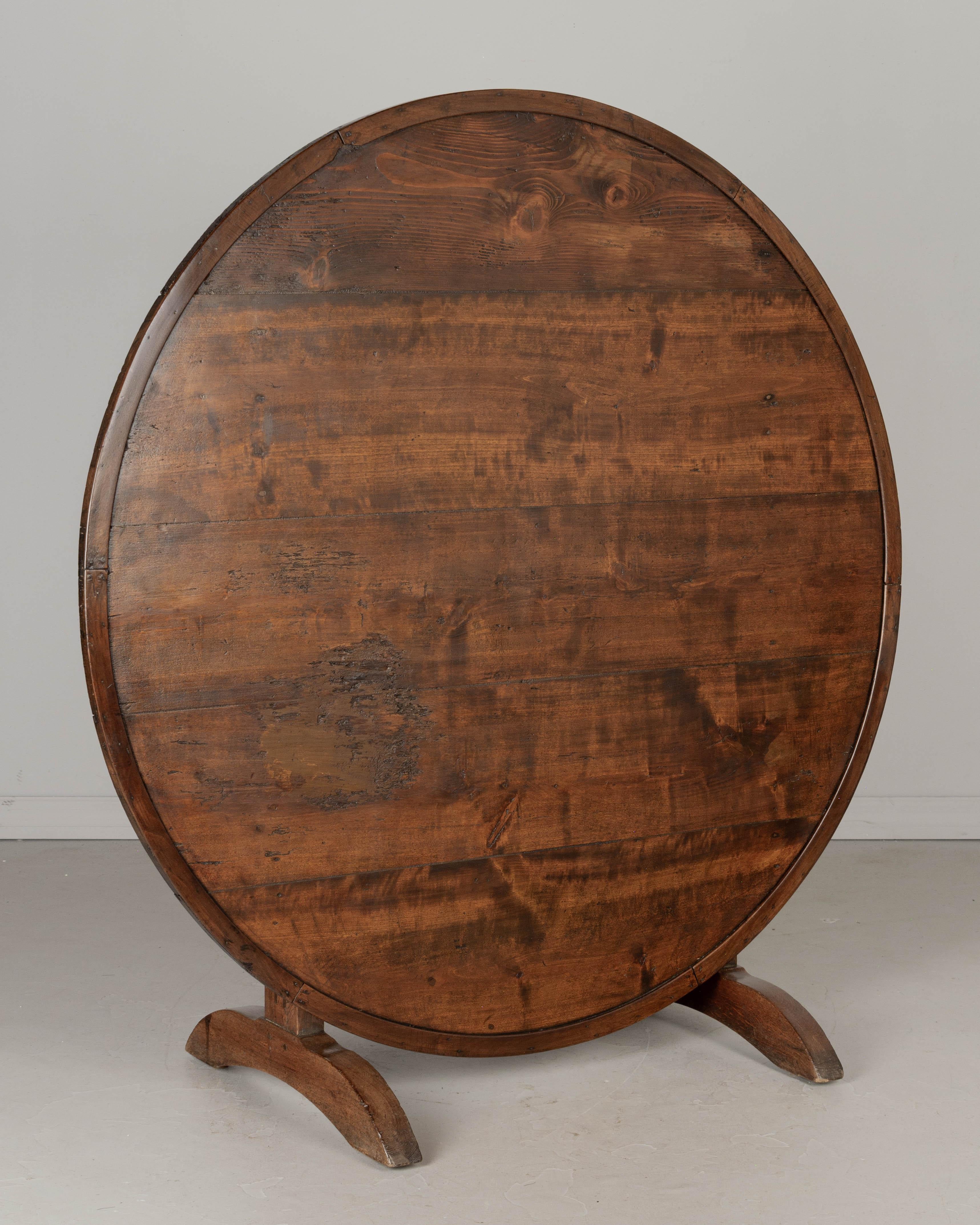 A large 19th century French wine tasting, or tilt-top table with pine plank top, sturdy solid oak base and walnut banding around the edge. Well-crafted with mortise and tenon joints and pegged construction. Top has a rustic worn surface with a worn