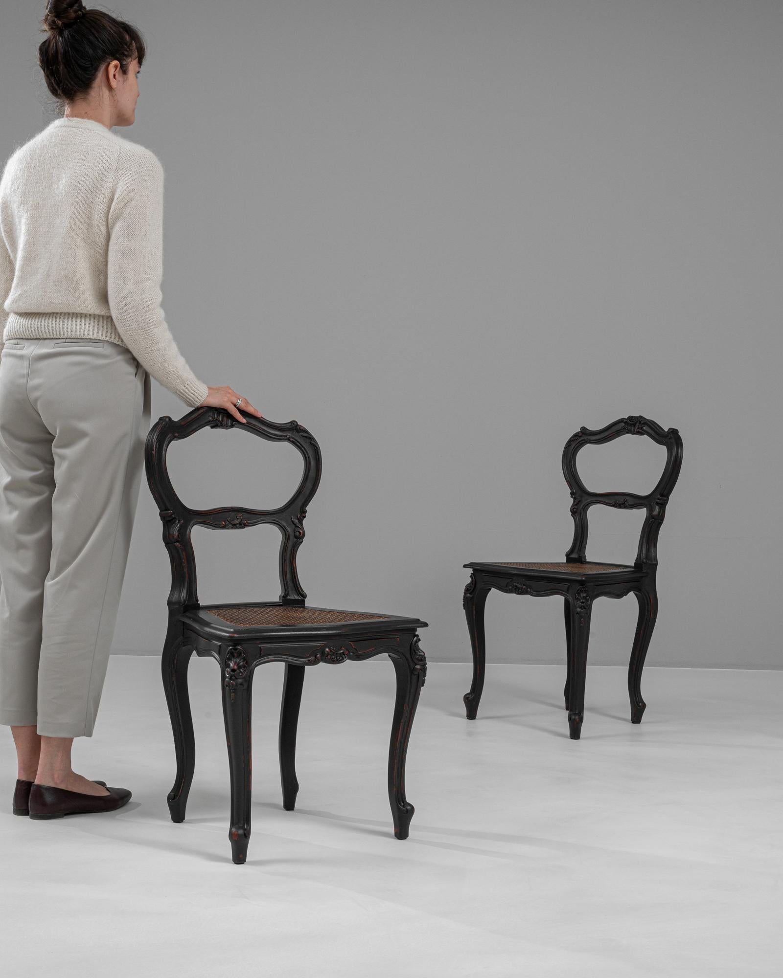 These exquisite 19th-century French wood chairs, finished in a striking black patina, offer an elegant and sophisticated addition to any space. The chairs boast a classic silhouette with graceful, curving lines that reflect the artful design of the