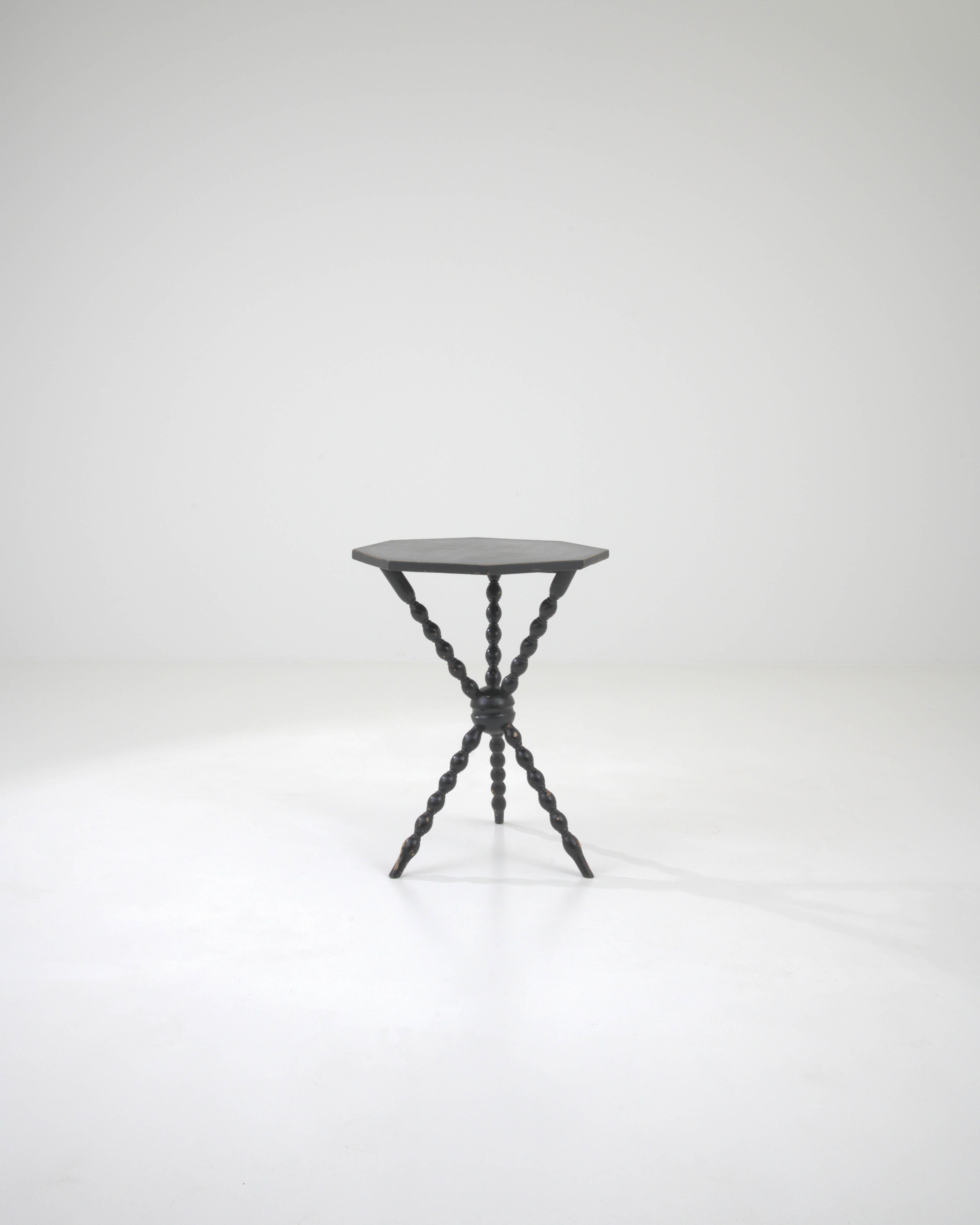Imbued with a sense of storied elegance, this 19th Century French Wood Side Table features a black patina that whispers tales of bygone sophistication. The octagonal top, edged with hints of wear, rests on a striking base of turned spindle legs that