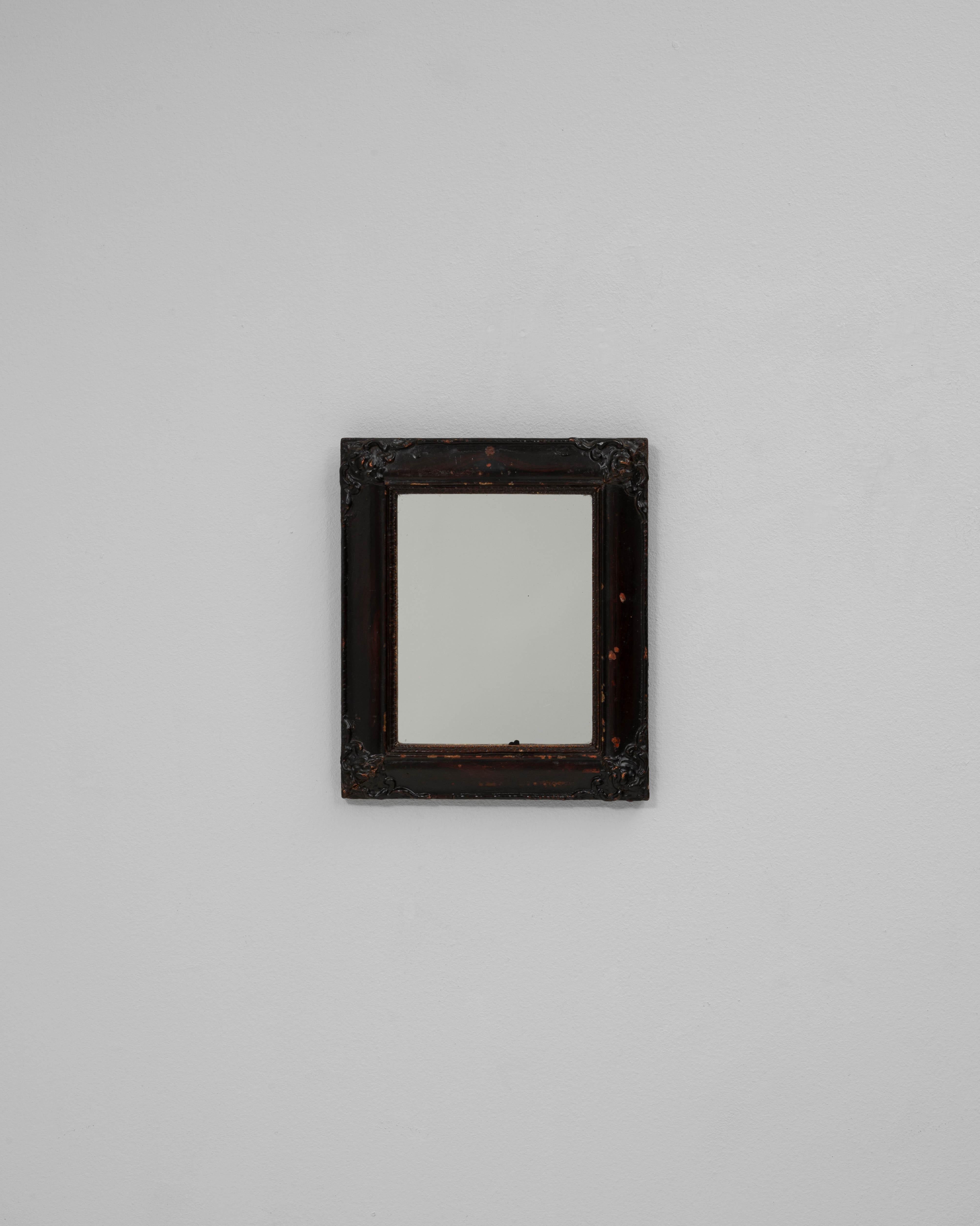Ce miroir mural en bois français du 19e siècle patiné noir dégage un charme intemporel et une élégance discrète. Encadré de bois richement sculpté avec de subtils embellissements floraux à chaque coin, il porte une belle patine noire vieillie qui