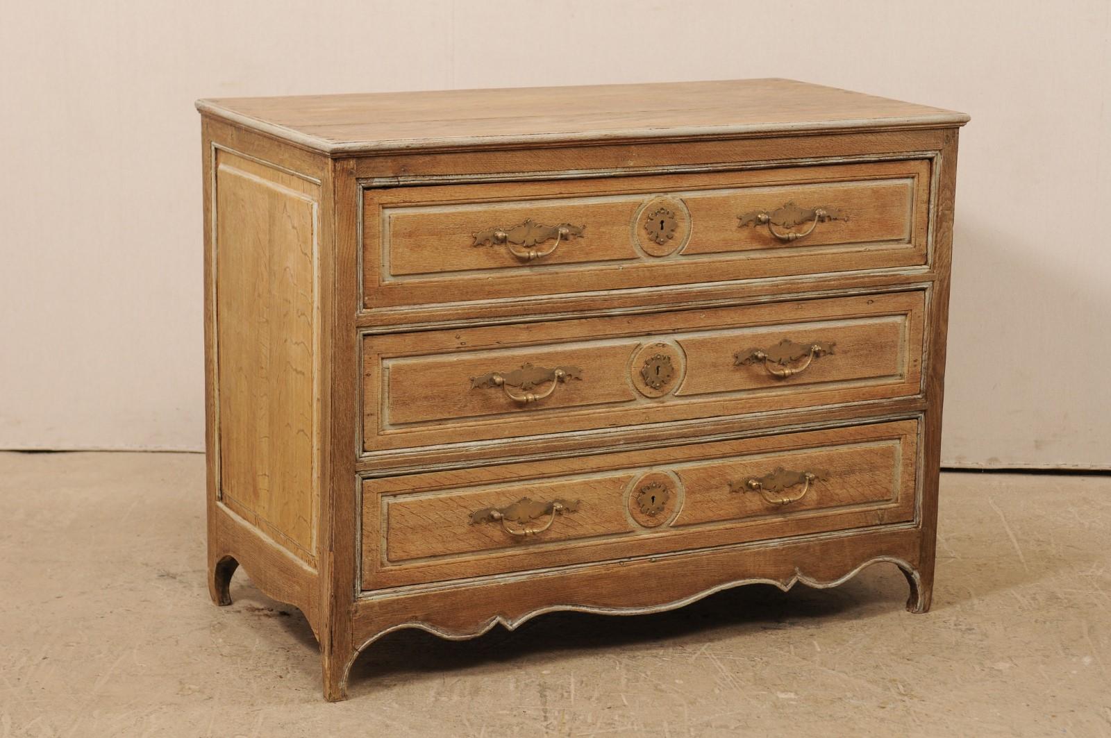 A French carved wood chest from the early 19th century. This antique commode from France features three decoratively paneled drawers with circular plaque carved at centre, single paneled sides, and scalloped skirt which flows down onto the slender