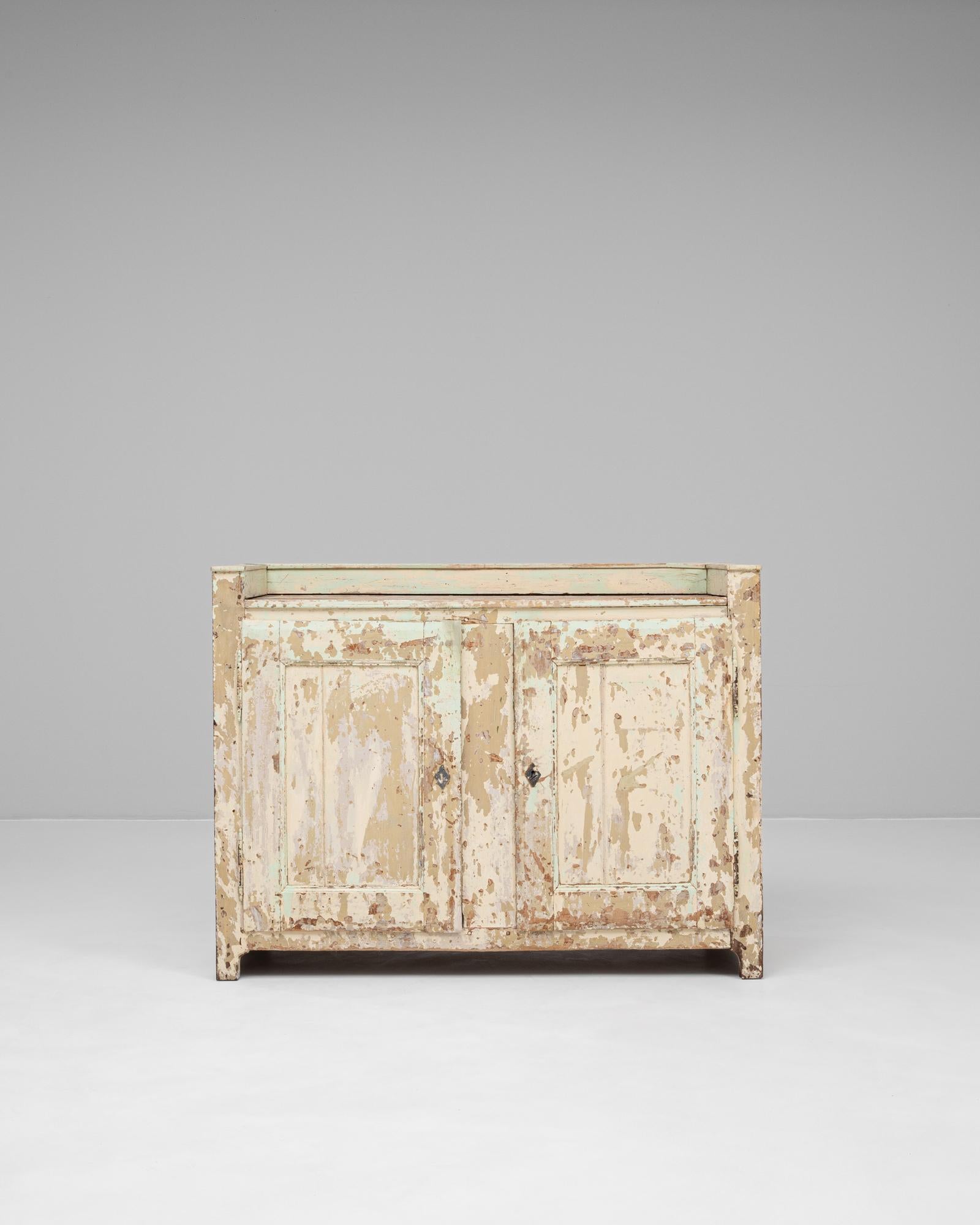 This 19th Century French wooden buffet features an exceptional patinated finish, showcasing layers of soft cream, pale green, and aged wood beneath a naturally distressed surface. Its raw, timeworn texture adds remarkable visual interest and
