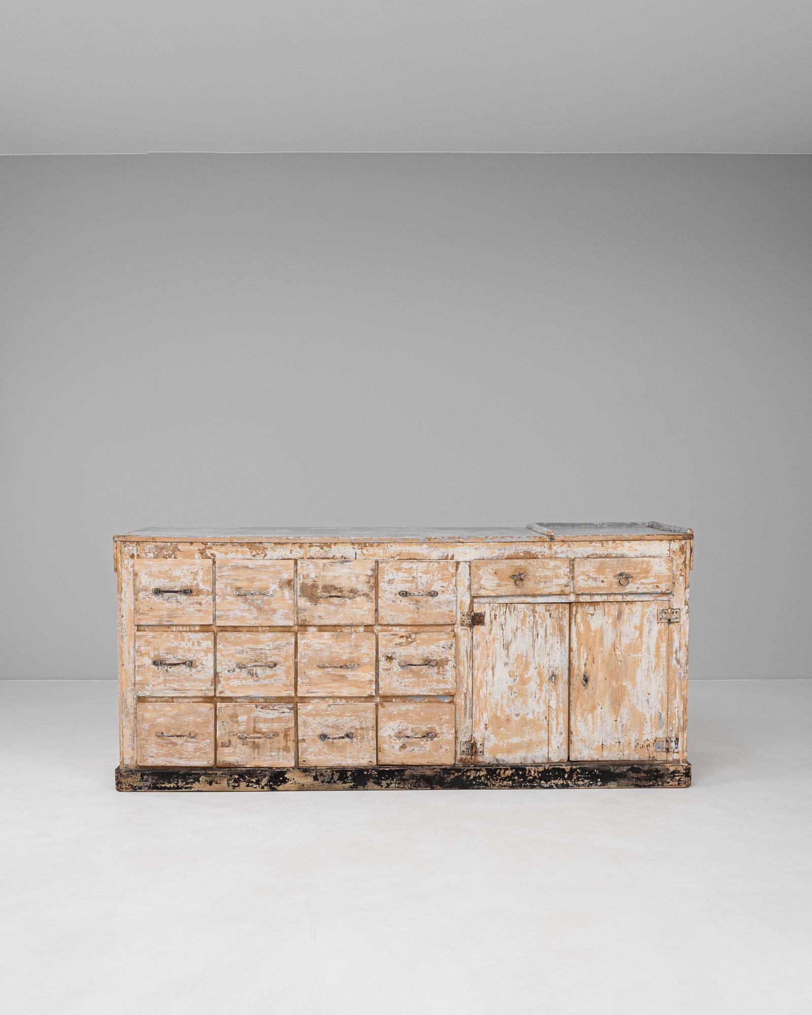 This 19th Century French shop counter is a striking example of utilitarian design infused with rustic charm. Crafted from solid wood, the piece features a heavily patinated surface with layers of original paint worn through over time, revealing a