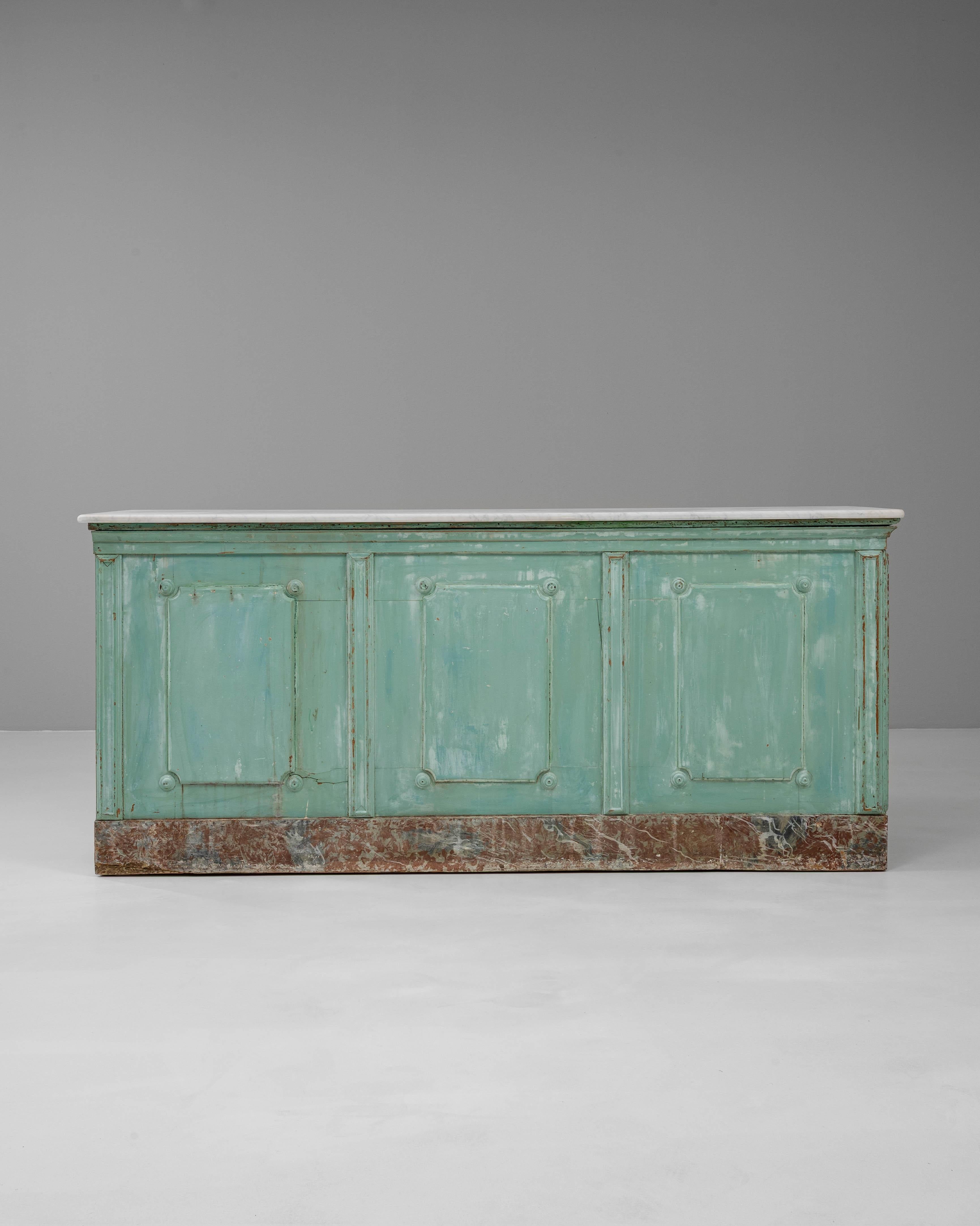 This 19th century French shop counter features its original patinated finish and a richly worn character that speaks to its history. The counter is topped with a white marble slab, offering a refined contrast to the painted wood base in layers of