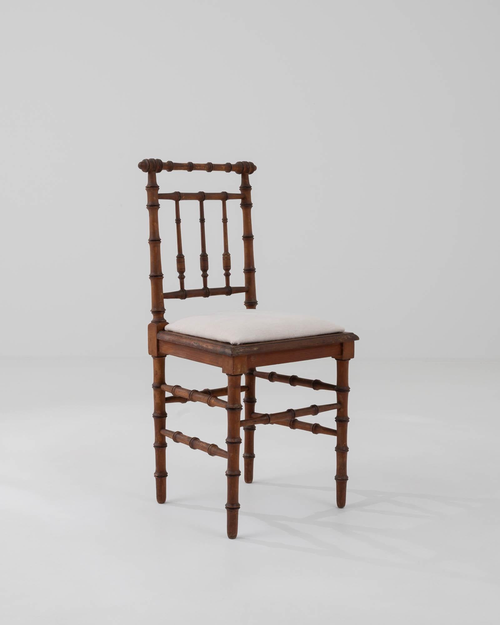 Embrace the charm of this 19th Century French wooden accent bistro chair, a delightful fusion of elegance and comfort. The chair features a distinctive spindle back and legs, reminiscent of bamboo, adding a touch of timeless appeal. The wooden frame