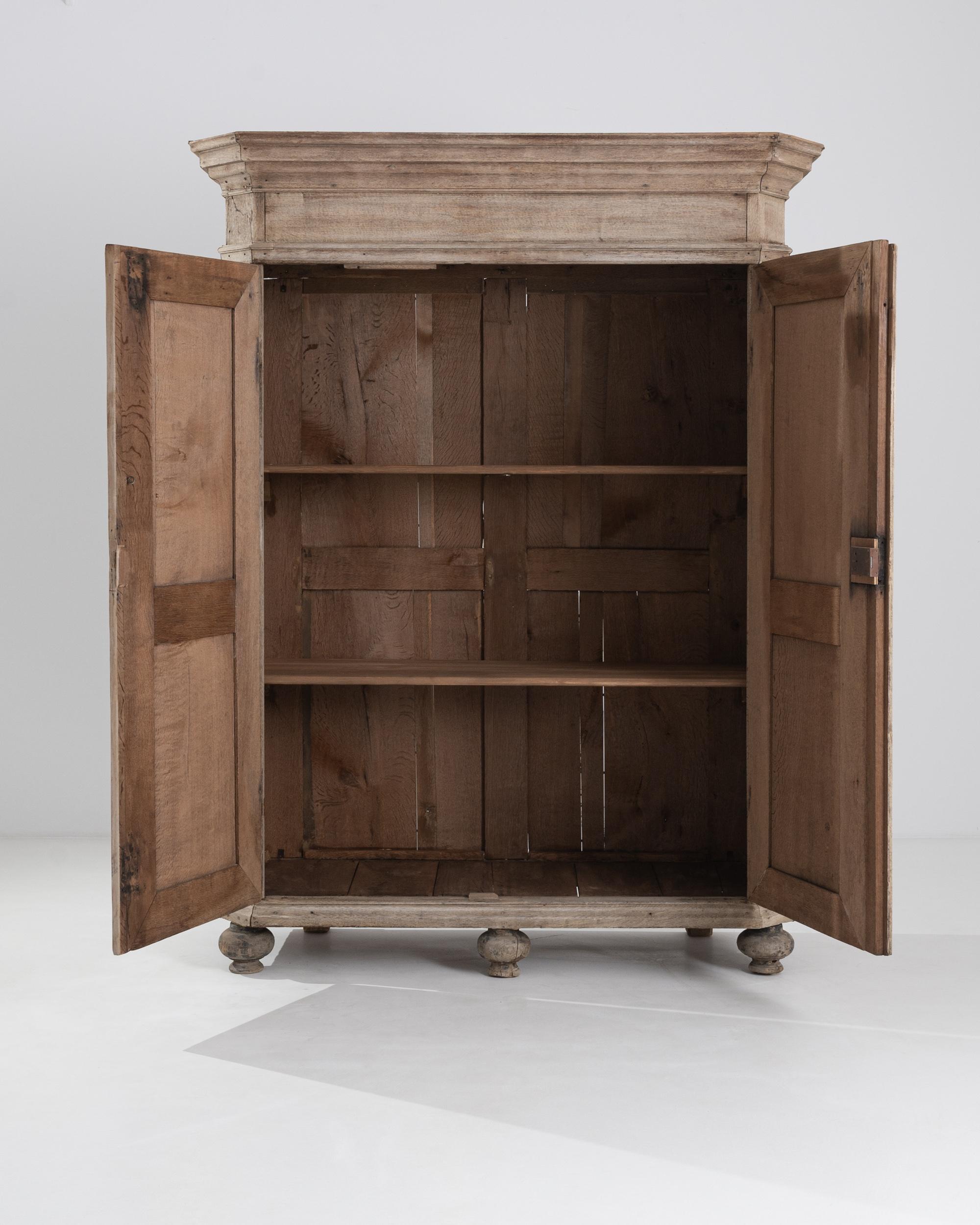 A vintage wooden armoire from France. This large cabinet opens its doors to reveal three sumptuous storage shelves. Artfully paneled doors and bulbous lathed feet engender a rustic sense of ease in this armoire. A delicate bleached oak finish and