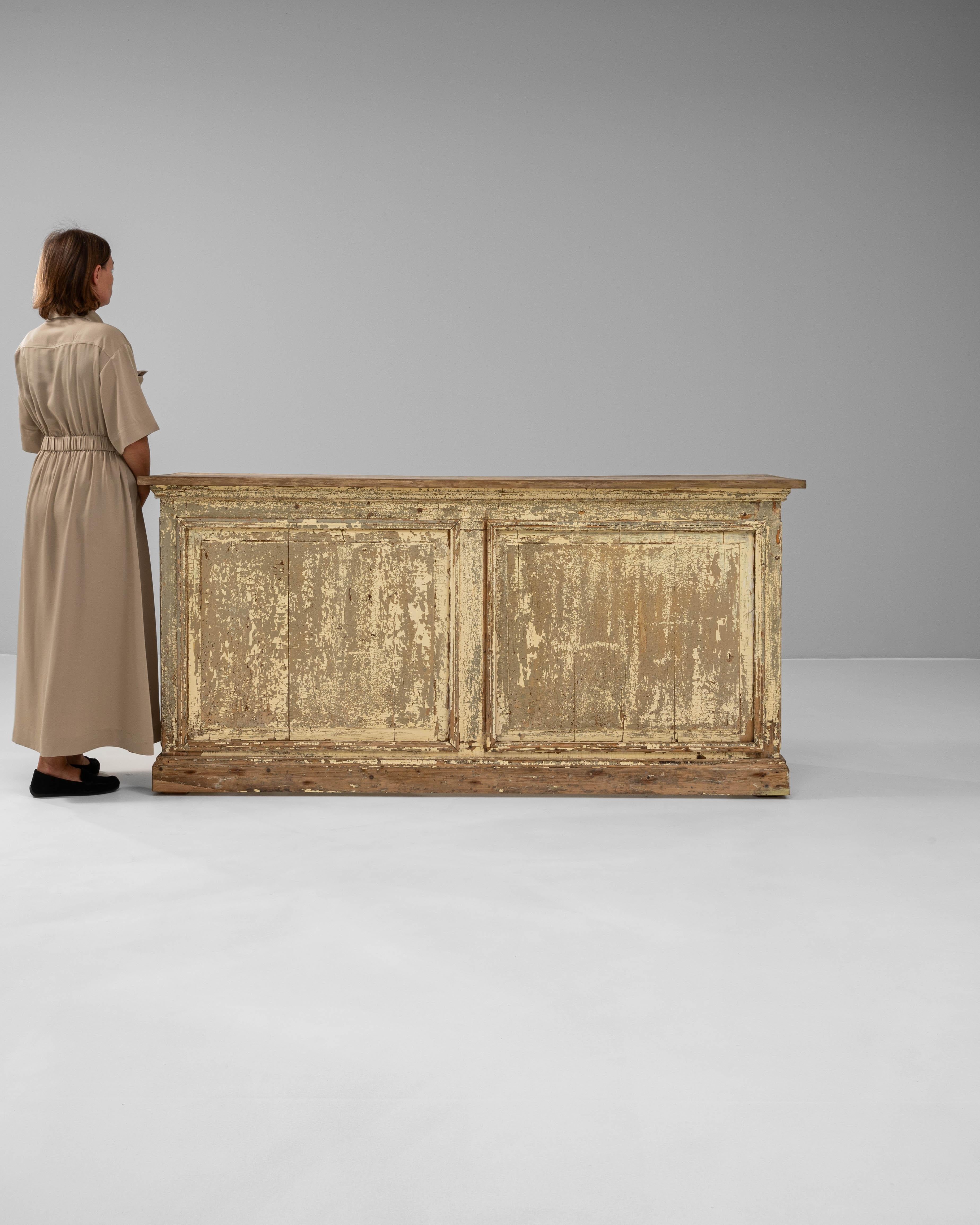 This 19th century French wooden bar boasts rustic authenticity and storied character, perfect for adding a touch of history to any space. Its original distressed paint reveals layers of time-worn patina, giving the piece a warm, lived-in appeal. The