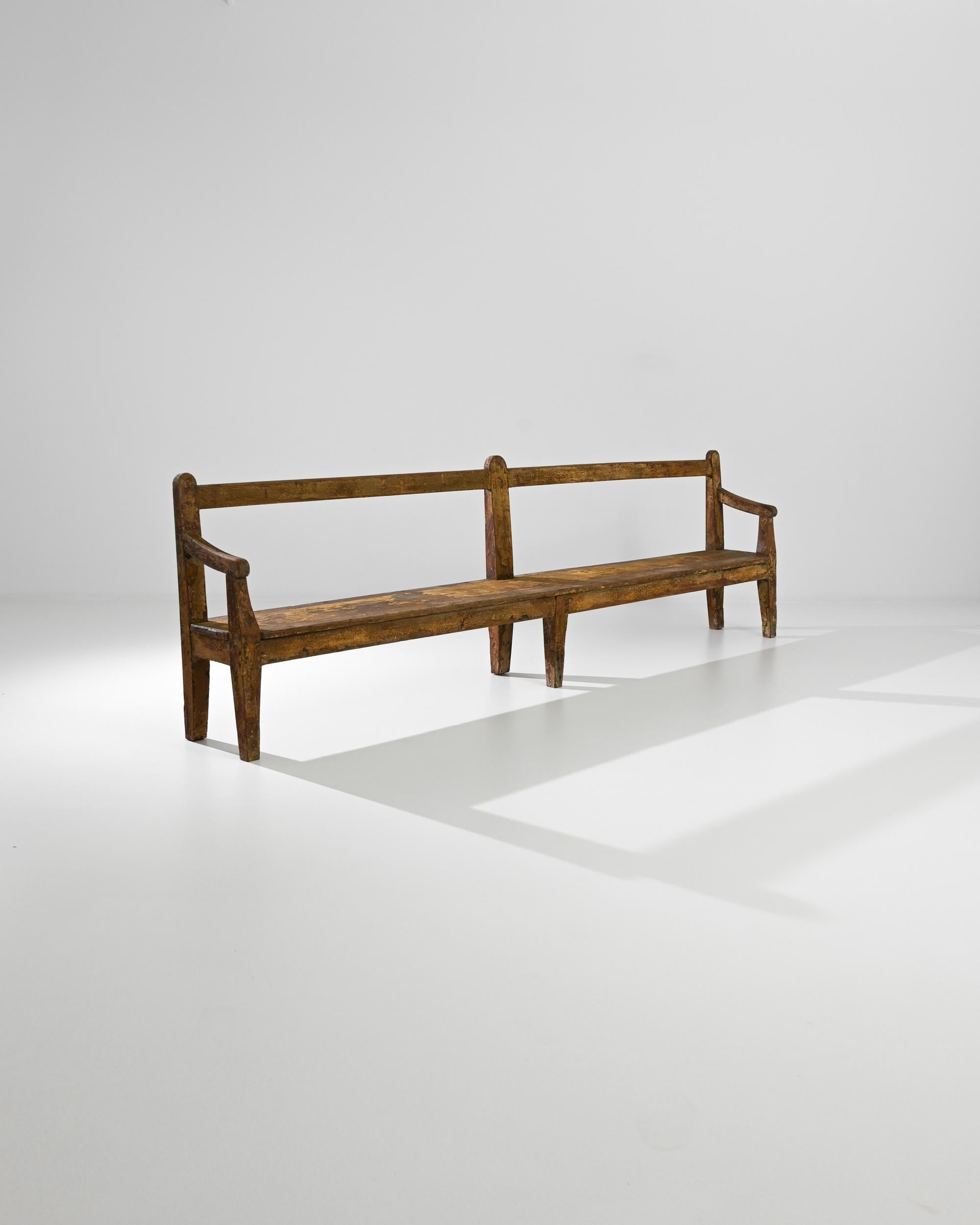 An antique wooden bench from 19th century France. Reminiscent of a park bench or church pew, the silhouette offers a communal space which welcomes one and all to sit. Tapered legs and slanted armrests add refinement; the absence of back-slats or