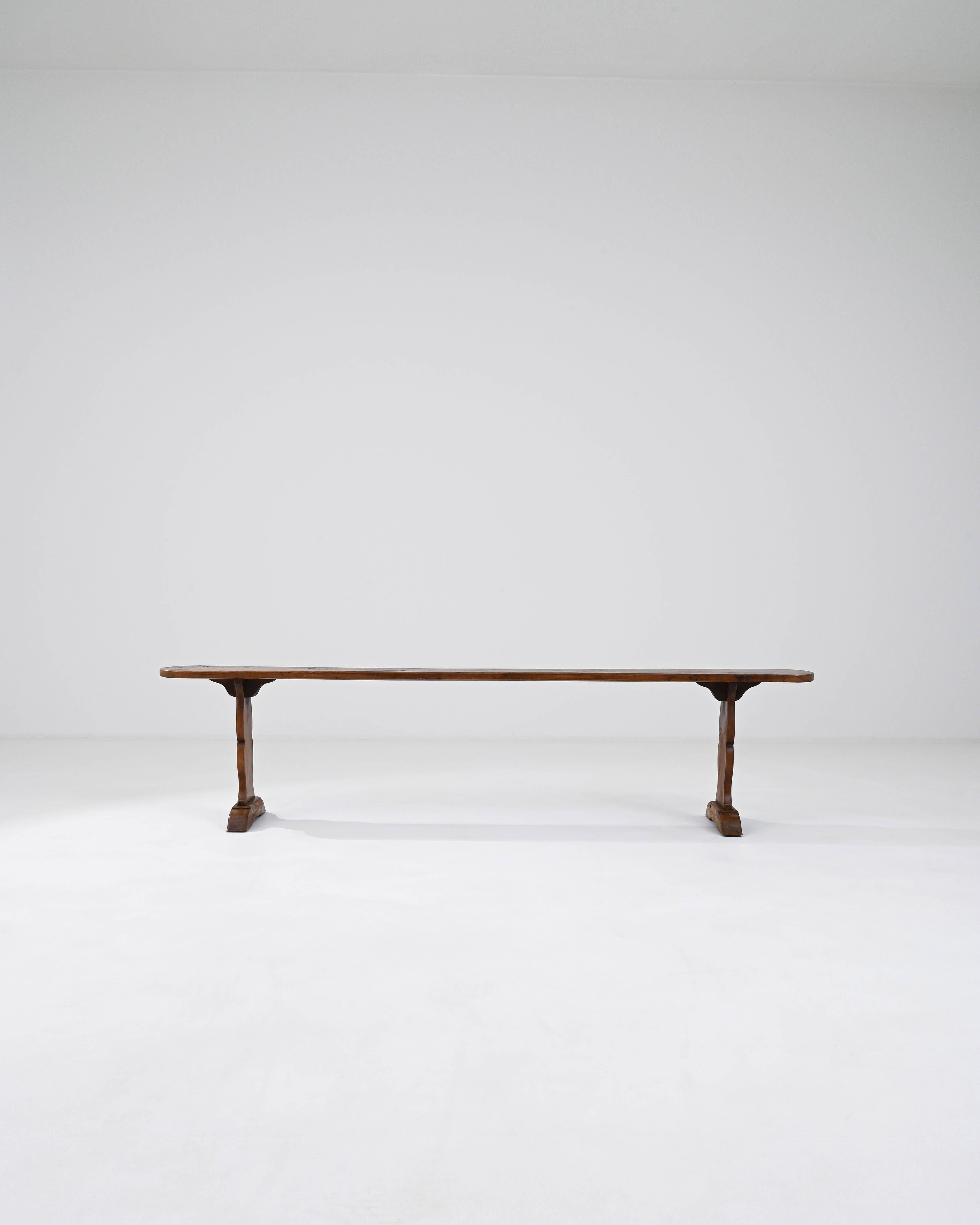 This 19th Century French Wooden Bench is an embodiment of rustic elegance and historical charm. Crafted from solid wood, it stands testament to the craftsmanship of the era with its sturdy trestle base and gracefully curved legs that anchor it