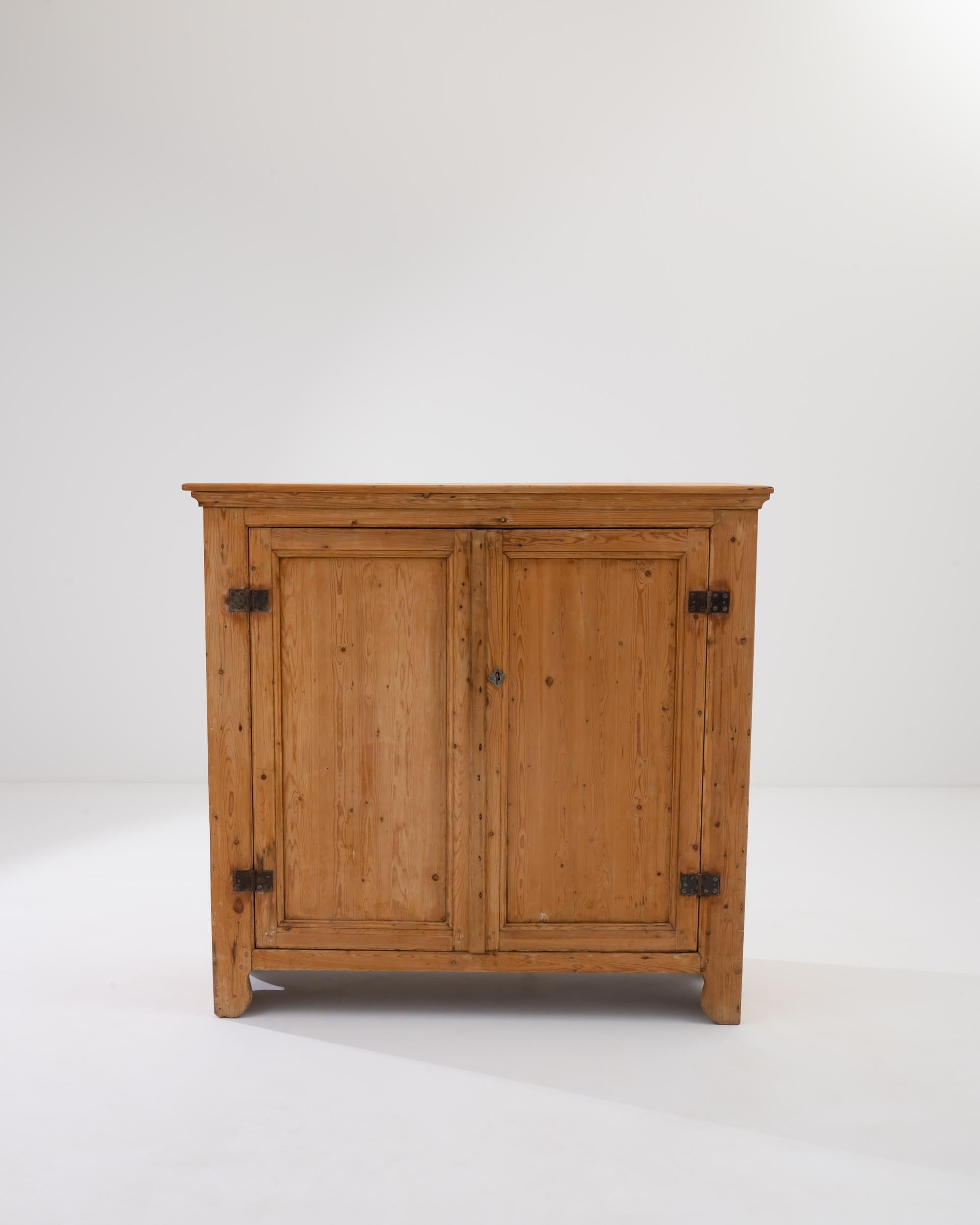 A wooden cabinet from 19th century France. Twin doors swing outwards to reveal three storage compartments, whose pale color contrasts pleasantly with the sunny golden brown of the cabinet’s exterior. A time-worn patina covers both the inside and out