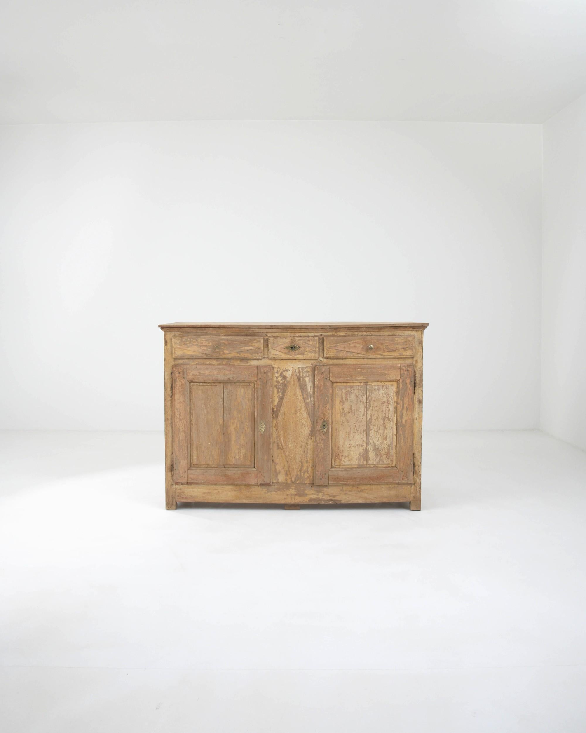 Made in France during the 19th century, this wooden buffet features three drawers resting above two square-panel doors, revealing ample compartments within. The rhombus carvings in the center elegantly complement the brass locks, adding an artistic