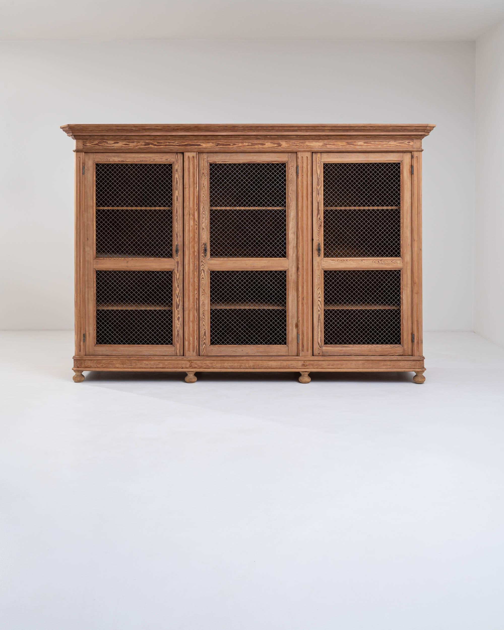 A wooden cabinet made in the 19th century in France. Crisscrossing metal forms a permeable barrier to the dozen storage compartments of this wooden cabinet. Mesh doors were once a common feature to allow airflow into linen cabinets or larders. The