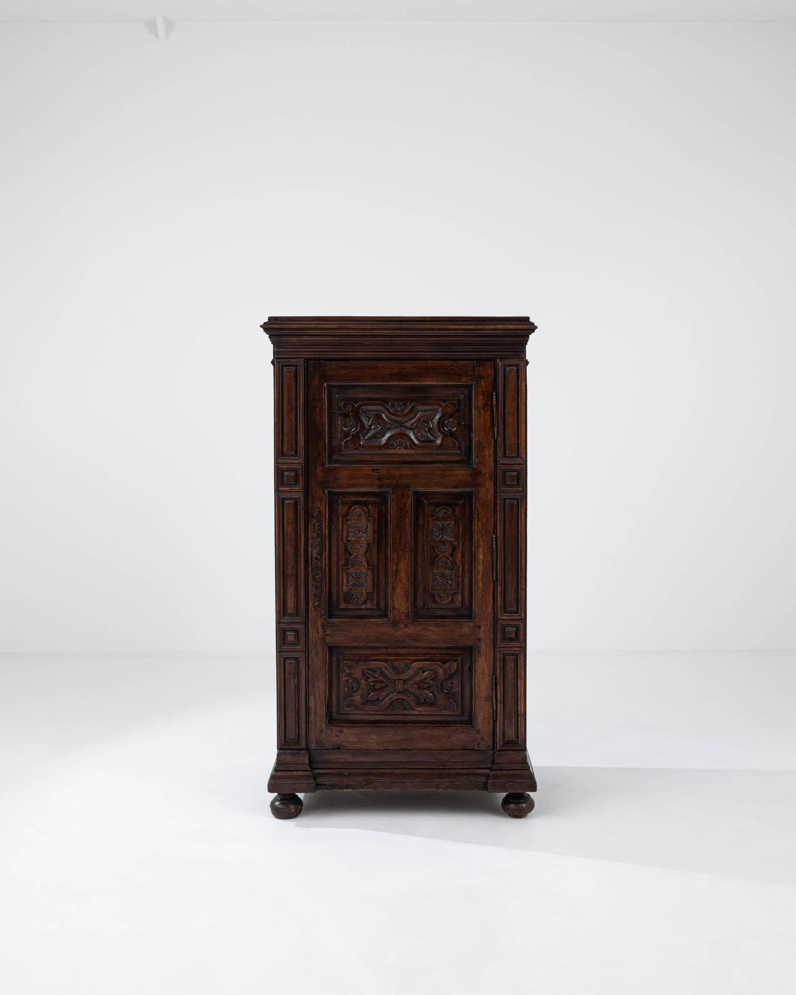 This 19th Century French Wooden Cabinet is a masterpiece of classic design, boasting the original patina that whispers tales of the past. The deep, lustrous tones of the wood are accented by intricate carvings that adorn each panel, featuring motifs