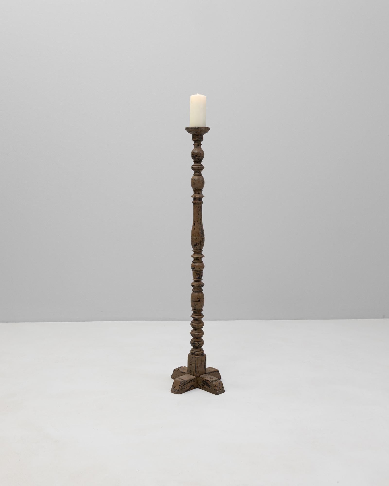 Candeliere in legno francese del XIX secolo con una bella forma a balaustro tornita e una patina ricca e invecchiata. Realizzato in legno massiccio, il pezzo poggia su una base a forma di croce intagliata che offre stabilità ed equilibrio scultoreo.