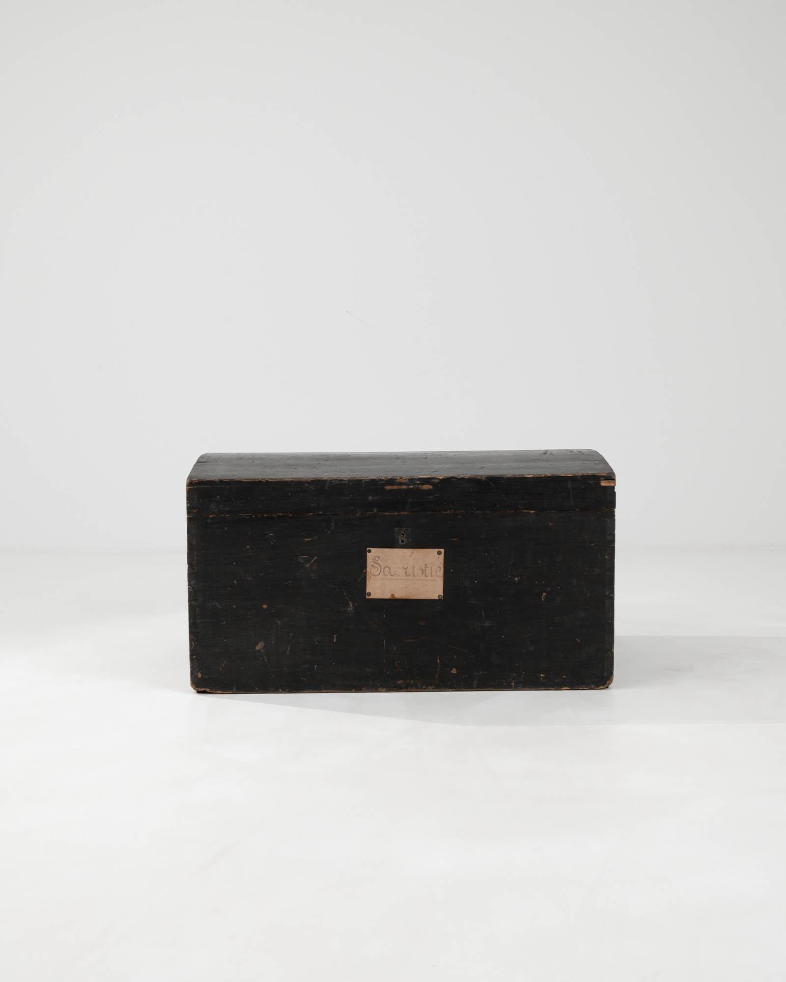 This 19th Century French Wooden Chest is a treasure trove of antiquity, offering a storied piece to store your cherished belongings. Its sturdy, time-worn exterior, dressed in a deeply patinated black finish, suggests a rich history and a life