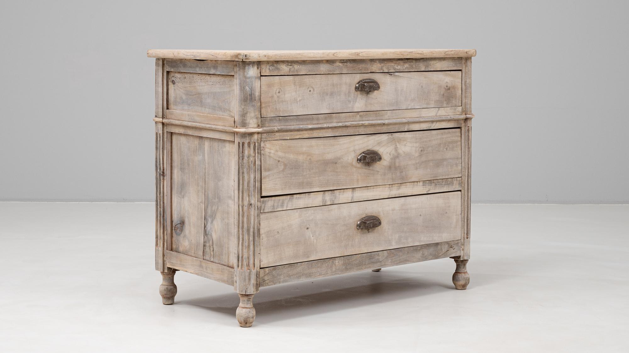 This 19th century French wooden chest of drawers offers understated elegance with its classic lines and timeworn charm. Crafted from solid wood and gently bleached to a soft, natural finish, the chest features three spacious drawers, each adorned