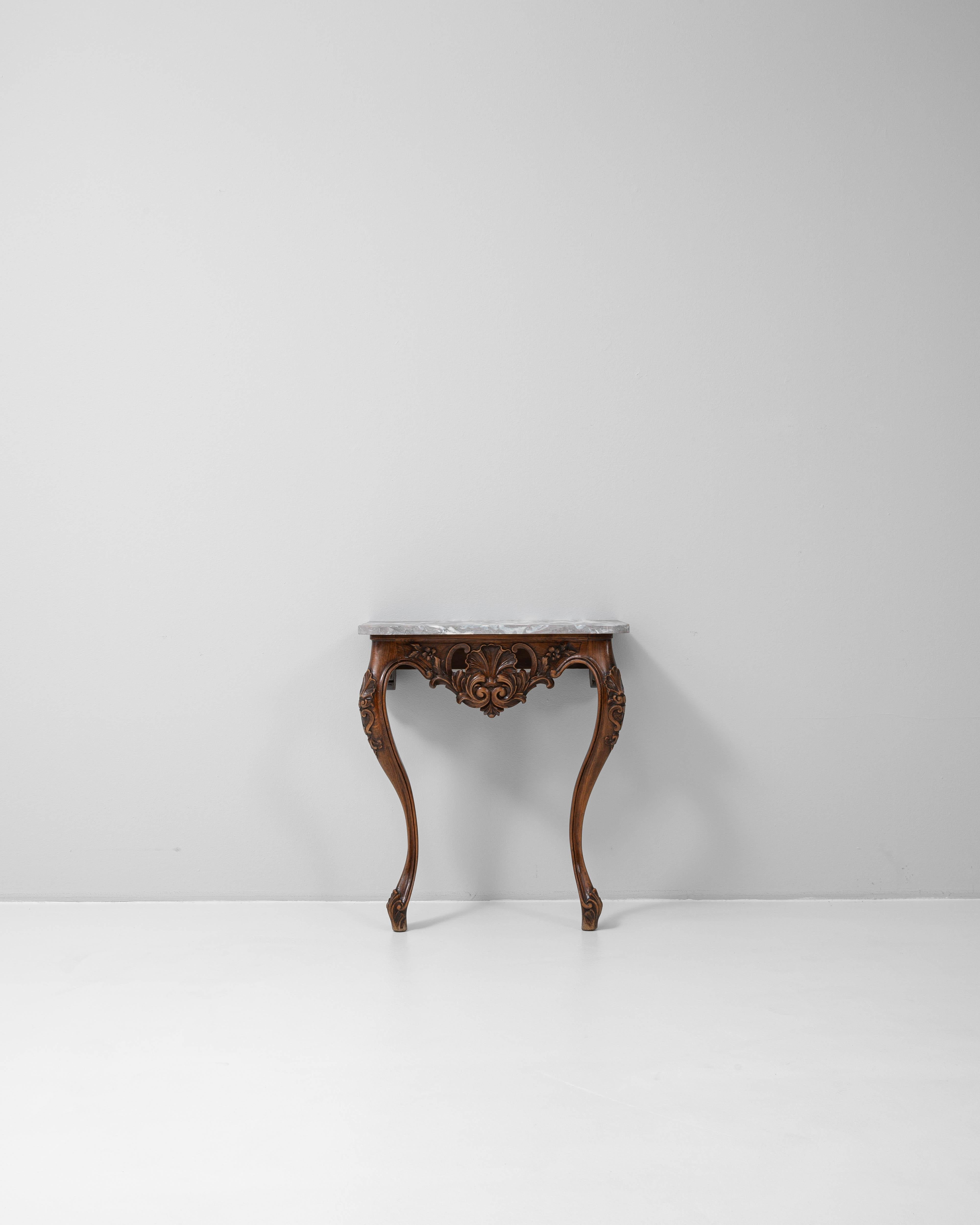 This 19th Century French console table is a striking example of Rococo-inspired craftsmanship, featuring an intricately hand-carved wooden base and a richly veined marble top. The apron is adorned with an elaborate shell and scroll motif, flanked by