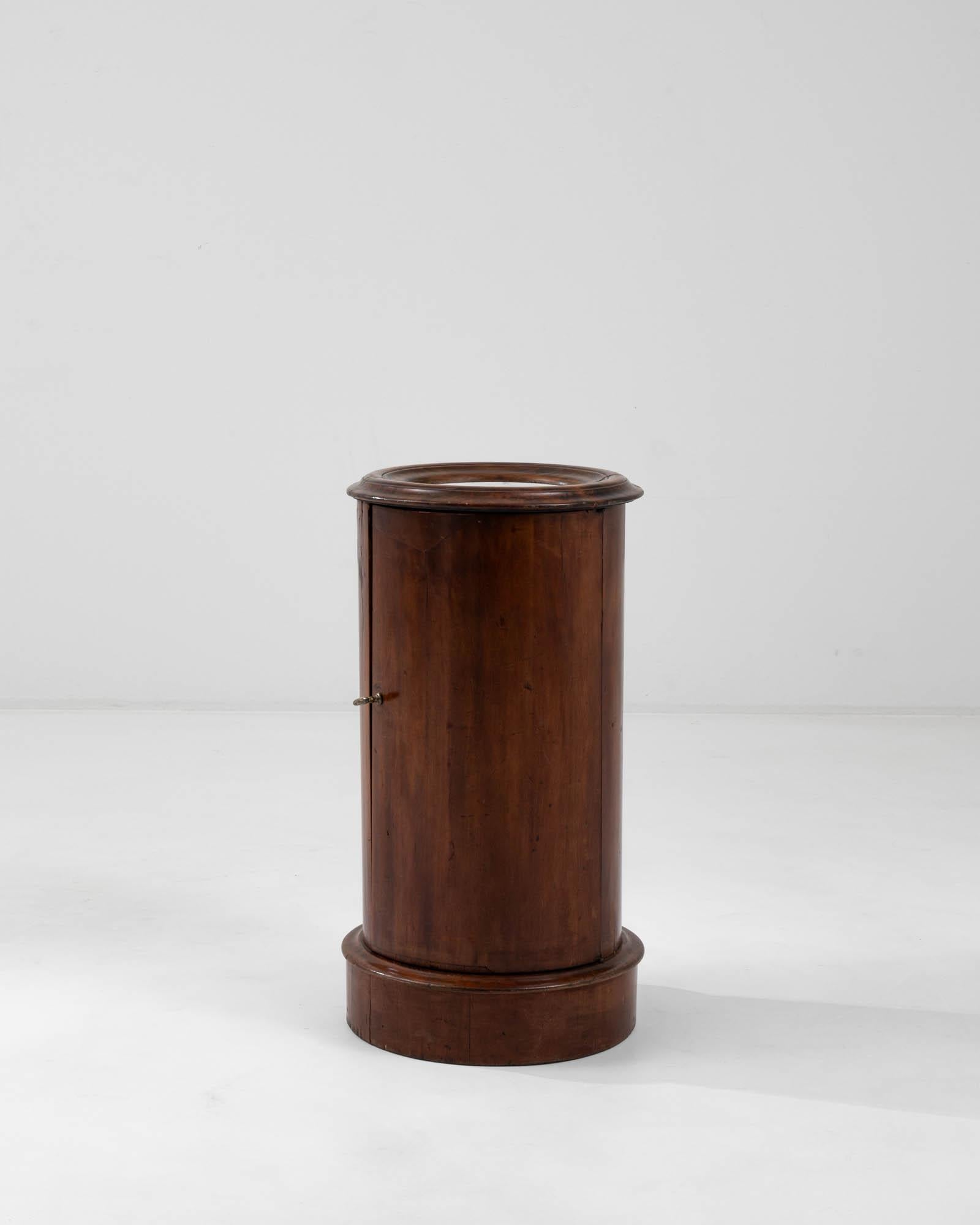 Boasting a sleek cylindrical shape, this elegant cabinet originates from 19th century France. An exquisite inset white marble top provides a striking contrast to the polished dark mahogany wood, skillfully accentuating its fluid contours. With a