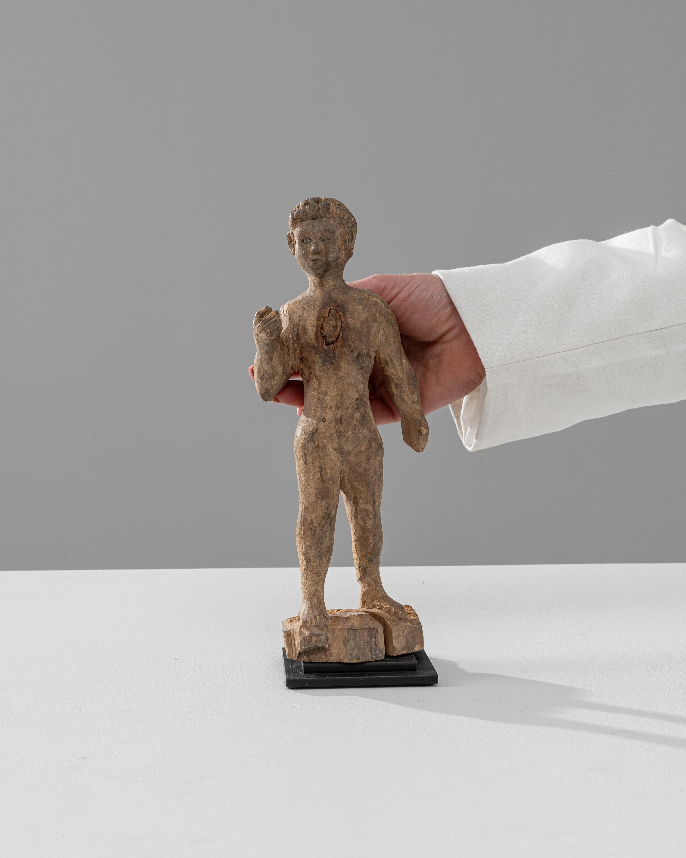 This charming 19th Century French Wooden Decoration on Metal Stand captures the essence of antique statuary and the enduring beauty of folk art. The figure, a carved wooden boy with a joyful expression and dynamic pose, stands on a simple yet
