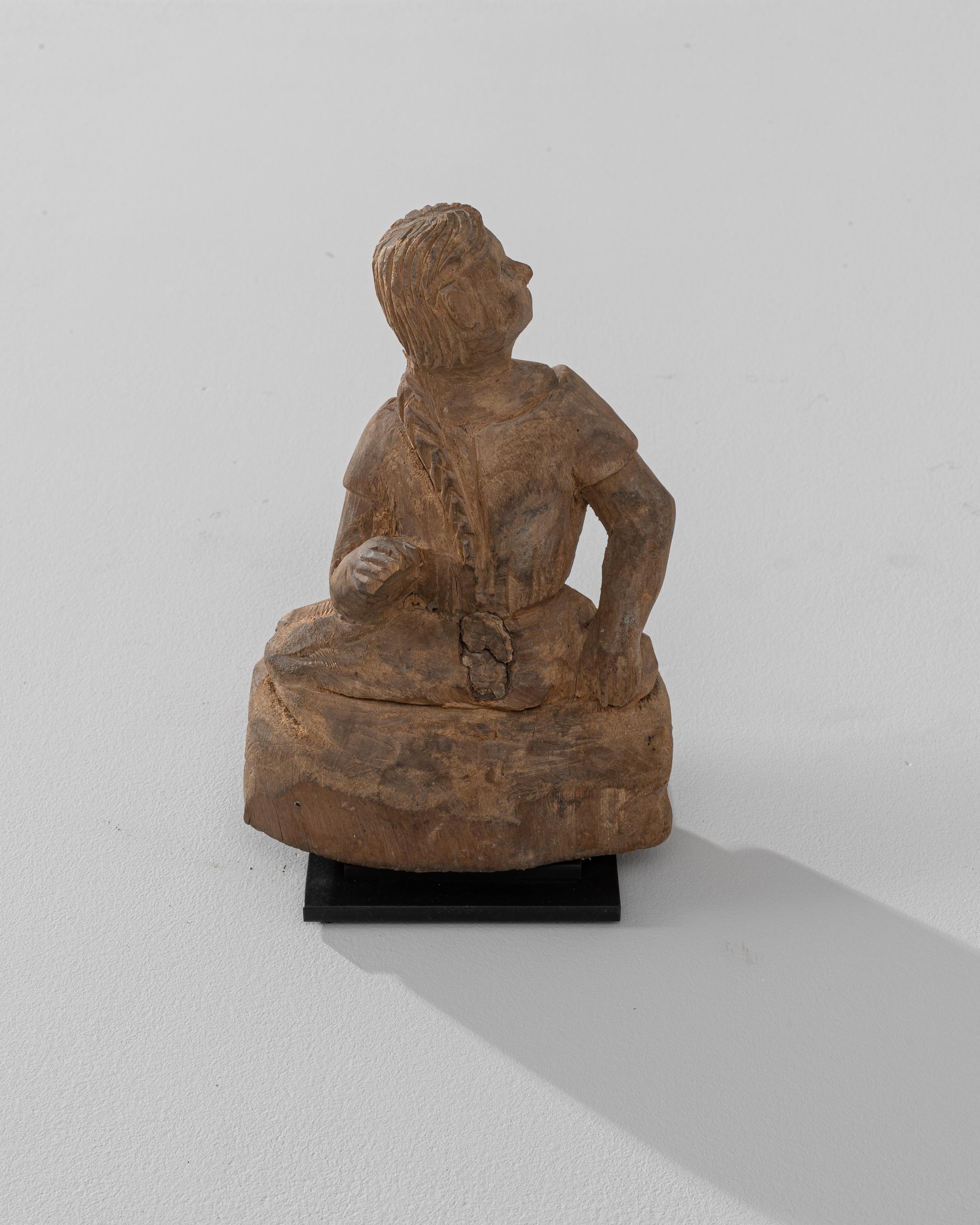 This 19th Century French Wooden Decoration on Metal Stand portrays a thoughtful, seated young girl, captured in a moment of quiet contemplation. The craftsmanship is evident in the detailed carving of her hair and clothing, bringing life and