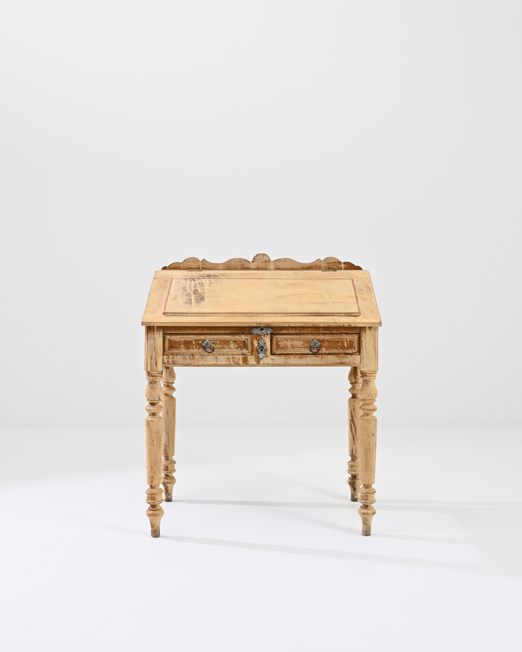 A wooden writing desk from 19th century France. The top of this desk opens up to reveal three storage compartments and a writing surface, below which sit two drawers. A sunny aura emits from the surface of this desk, a creamy peach colored patina