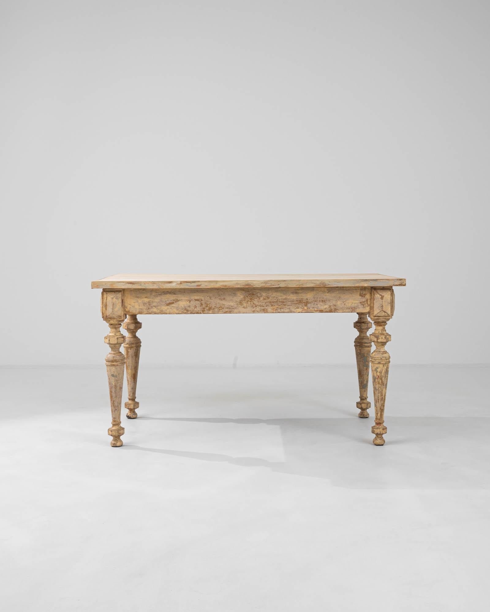 This 19th Century French wooden dining table is a remarkable testament to the timeless beauty of antique furniture. Its substantial surface, adorned with the gentle marks of time, stands upon elegantly carved legs whose deliberate distressing