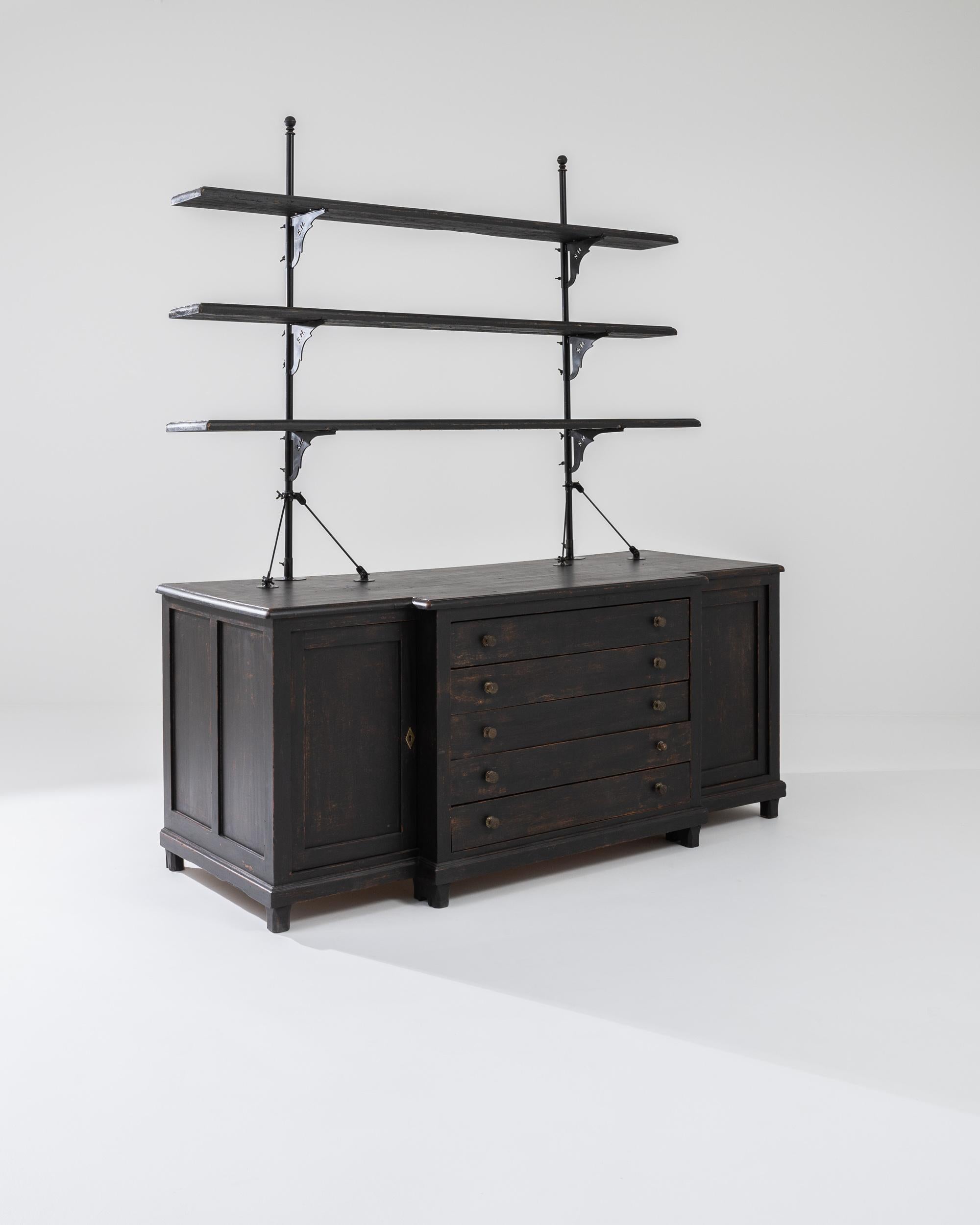 Rational and distinguished, this antique wooden display cabinet is a covetable find. Built in France in the 1800s, the airy, stripped-back composition of the upper shelves evokes the furled masts of ships, while the central drawers of the lower