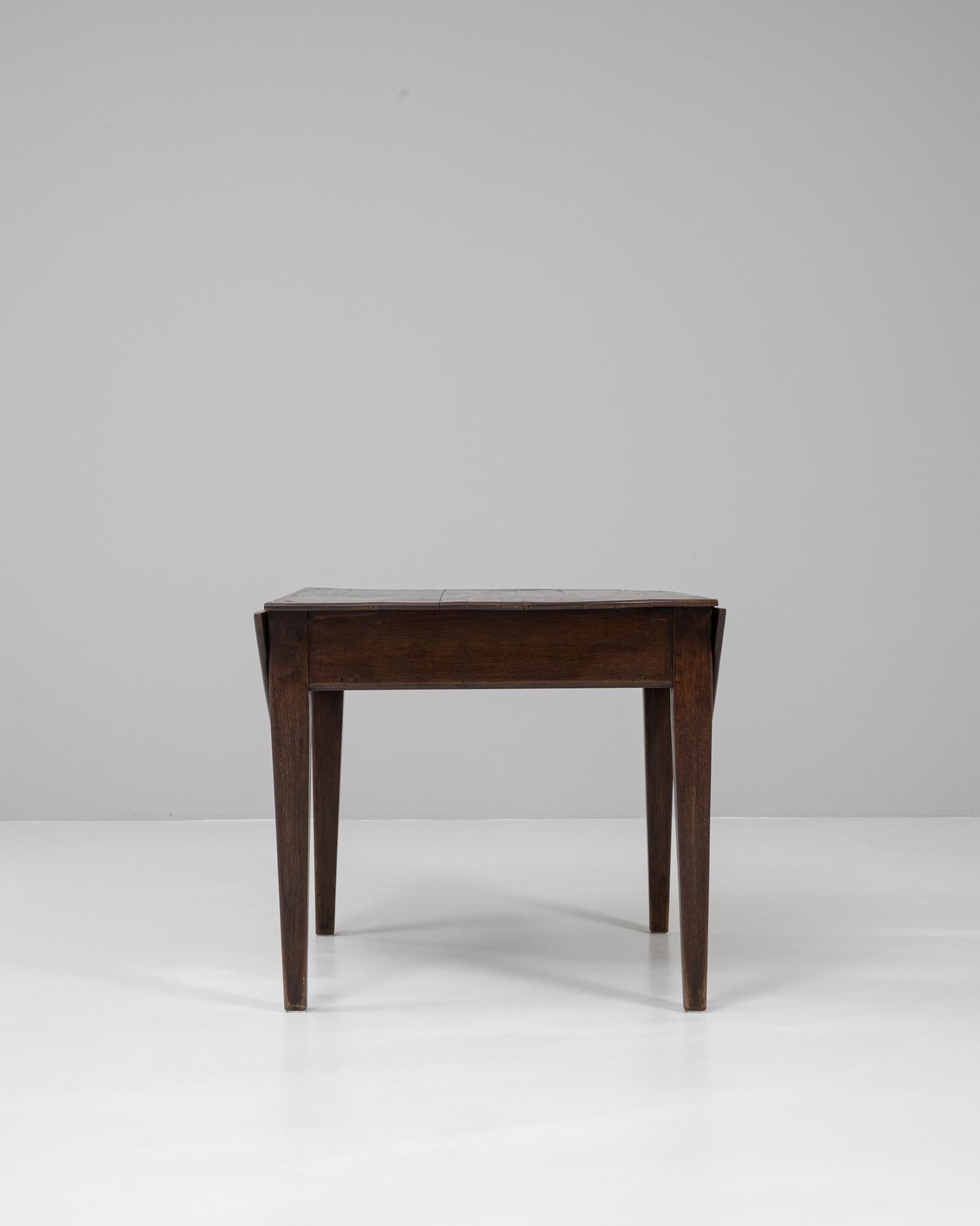 This 19th century French wooden drop-leaf table retains its original patina, showcasing a rich surface aged with time and use. Crafted with simple yet elegant lines, it features tapered legs and a sturdy rectangular frame, with hinged leaves that