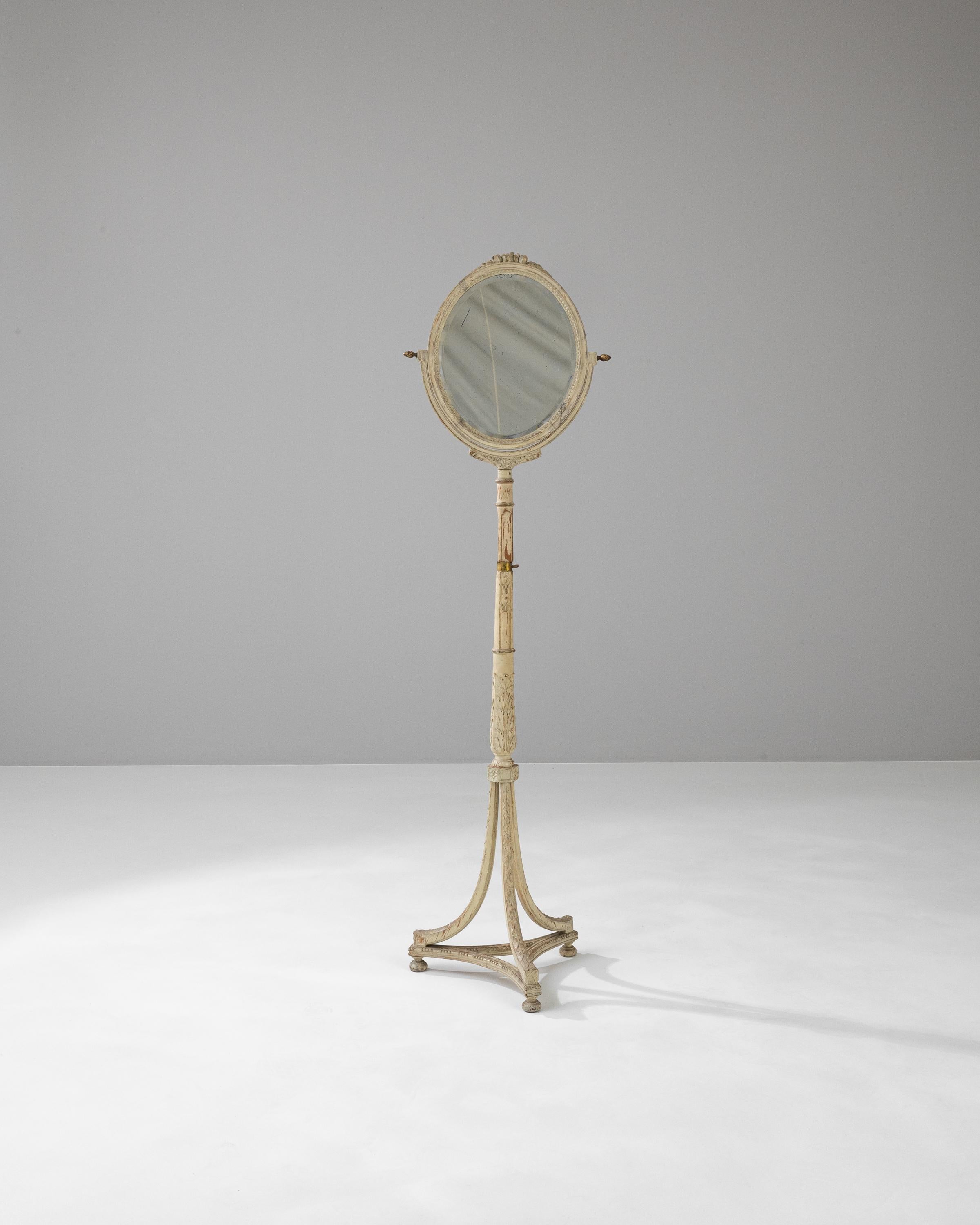 Versetzen Sie sich in die Eleganz des 19. Jahrhunderts zurück mit diesem exquisiten französischen Holzbodenspiegel. Die anmutig gealterte weiße Patina hebt die filigranen Schnitzereien an Rahmen und Ständer hervor. Der längliche, ovale Spiegel ist