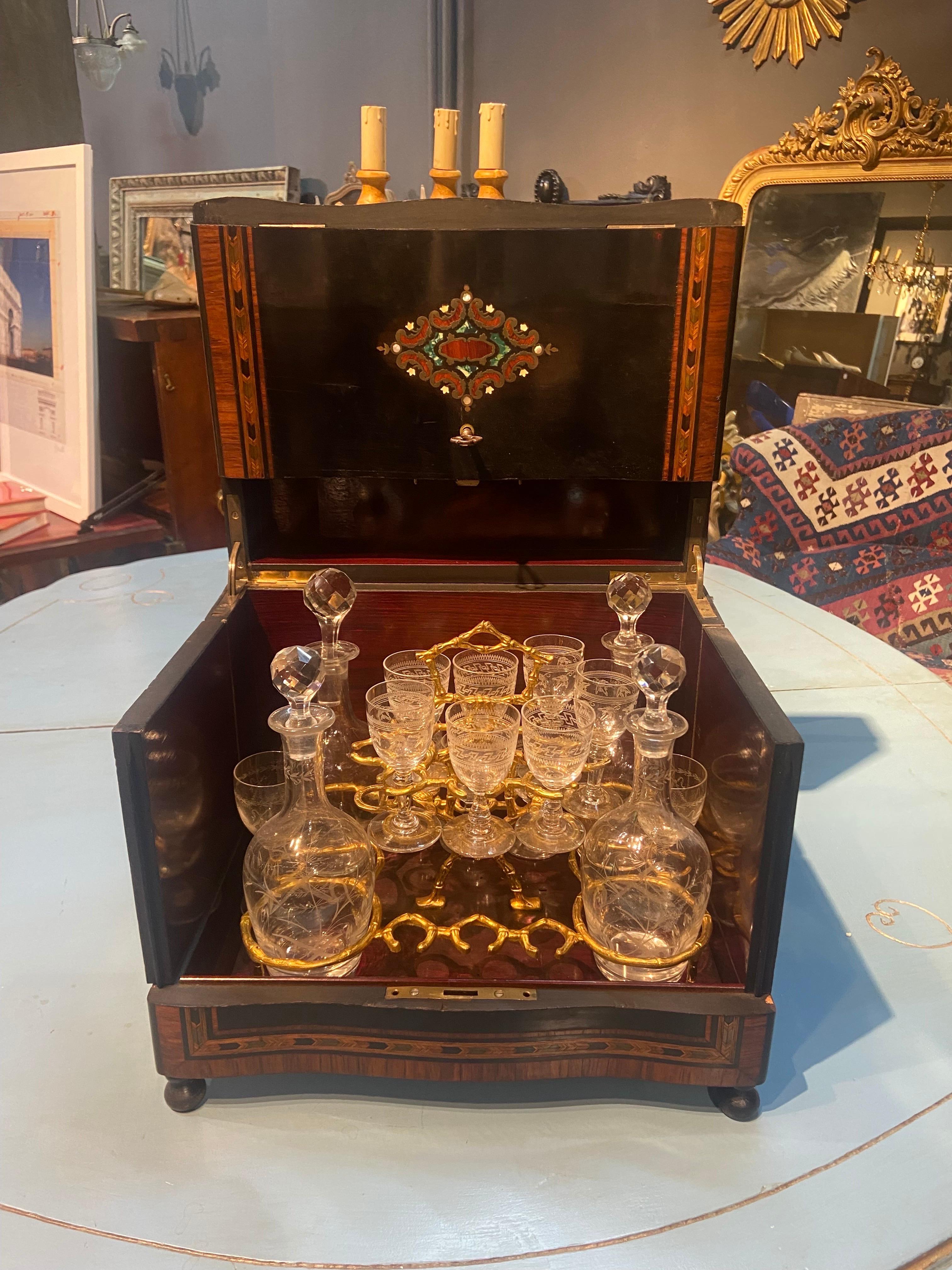 An wooden ebonised and hand-painted liquor cabinet in Napoleon III style with brass inlay. Exterior opens in three directions to elegantly reveal a crystal service surrounded by polished rosewood. It contains four crystal carafes with stoppers and