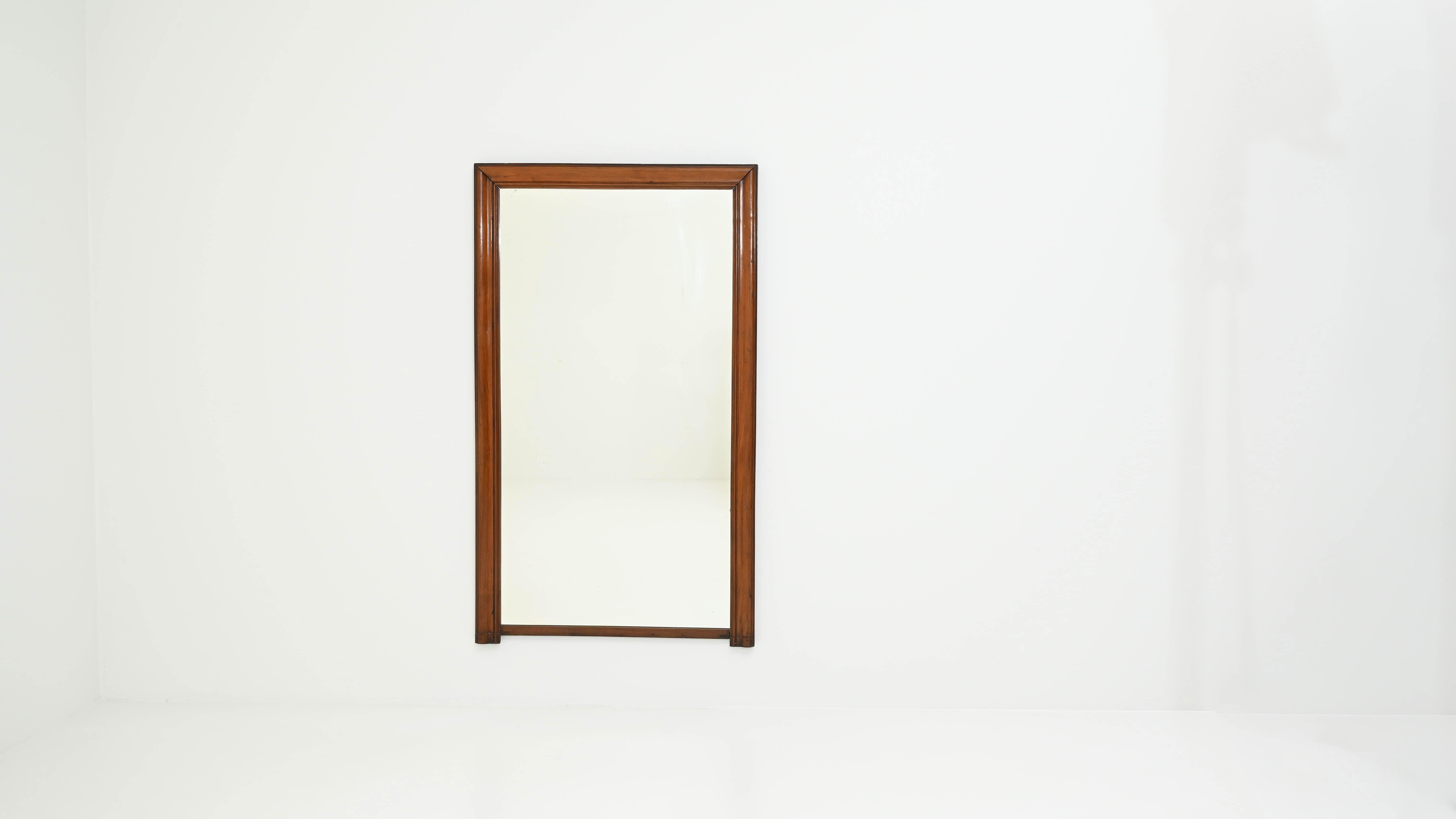 The understated silhouette of this 19th-century mirror, made in France, is shaped by the elegant rectangular frame with protruding bottom corners and a thinner line along the lower edge. The warm amber hue of the polished wood brings a touch of