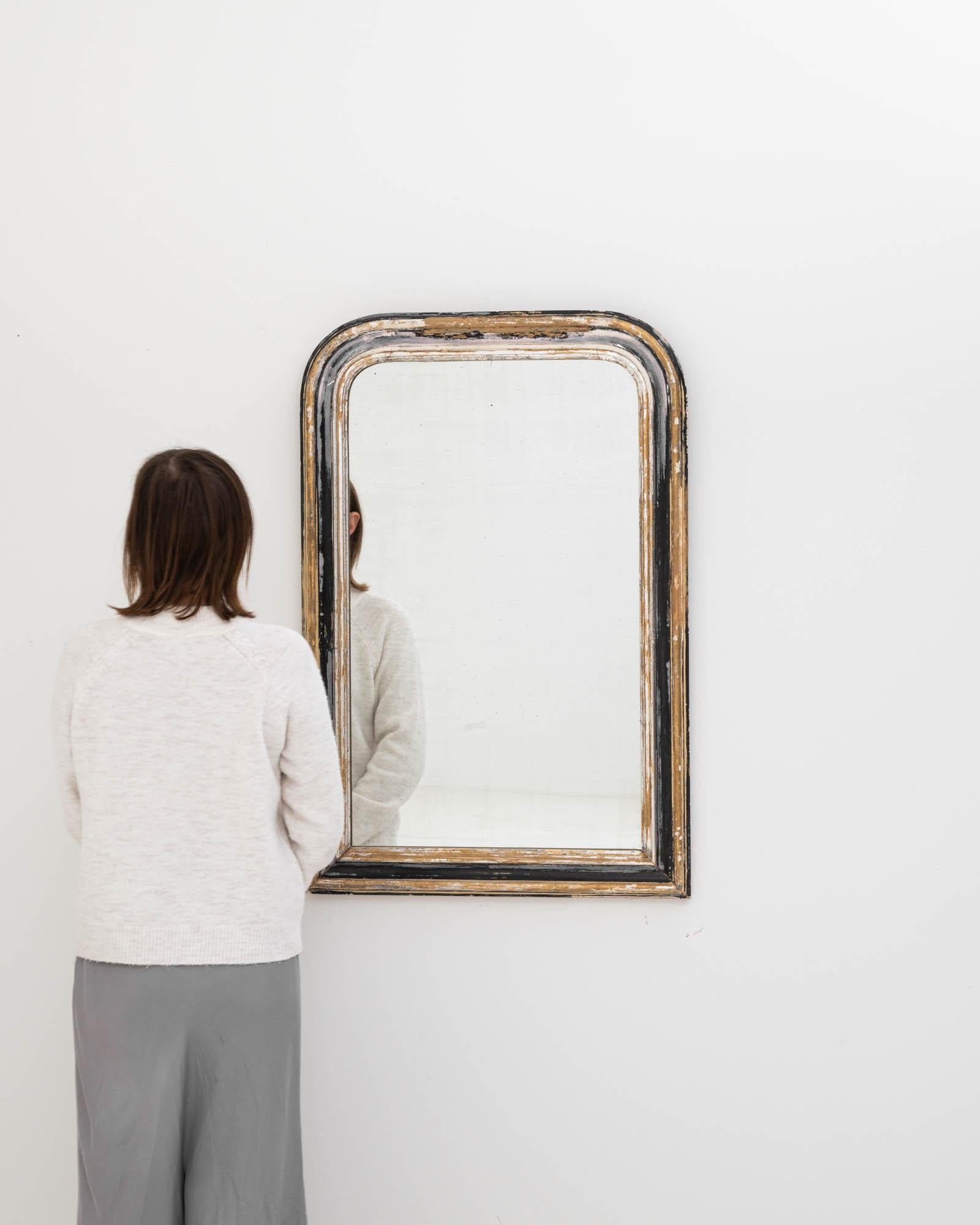 Immerse yourself in the vintage allure of this 19th Century French Wooden Mirror, a piece that effortlessly brings the charm of the past into the present. The frame, with its softly rounded edges and a worn gilt finish, showcases the genuine patina