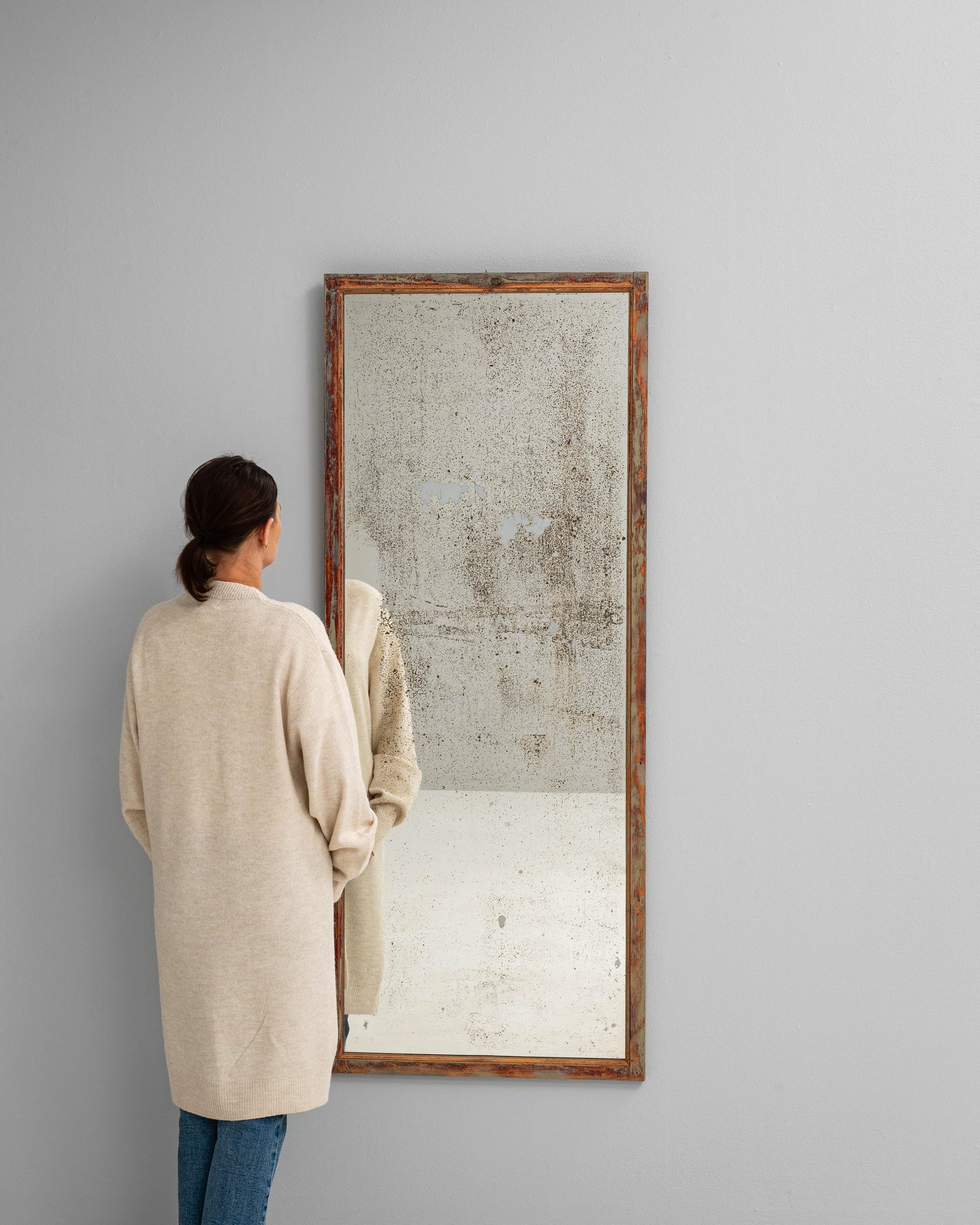 Este espejo francés de madera del siglo XIX tiene una sencilla forma rectangular con un marco desgastado por el tiempo que muestra capas de pintura desgastada en cálidos tonos terracota y salvia apagada. La pátina de la superficie se ha desarrollado