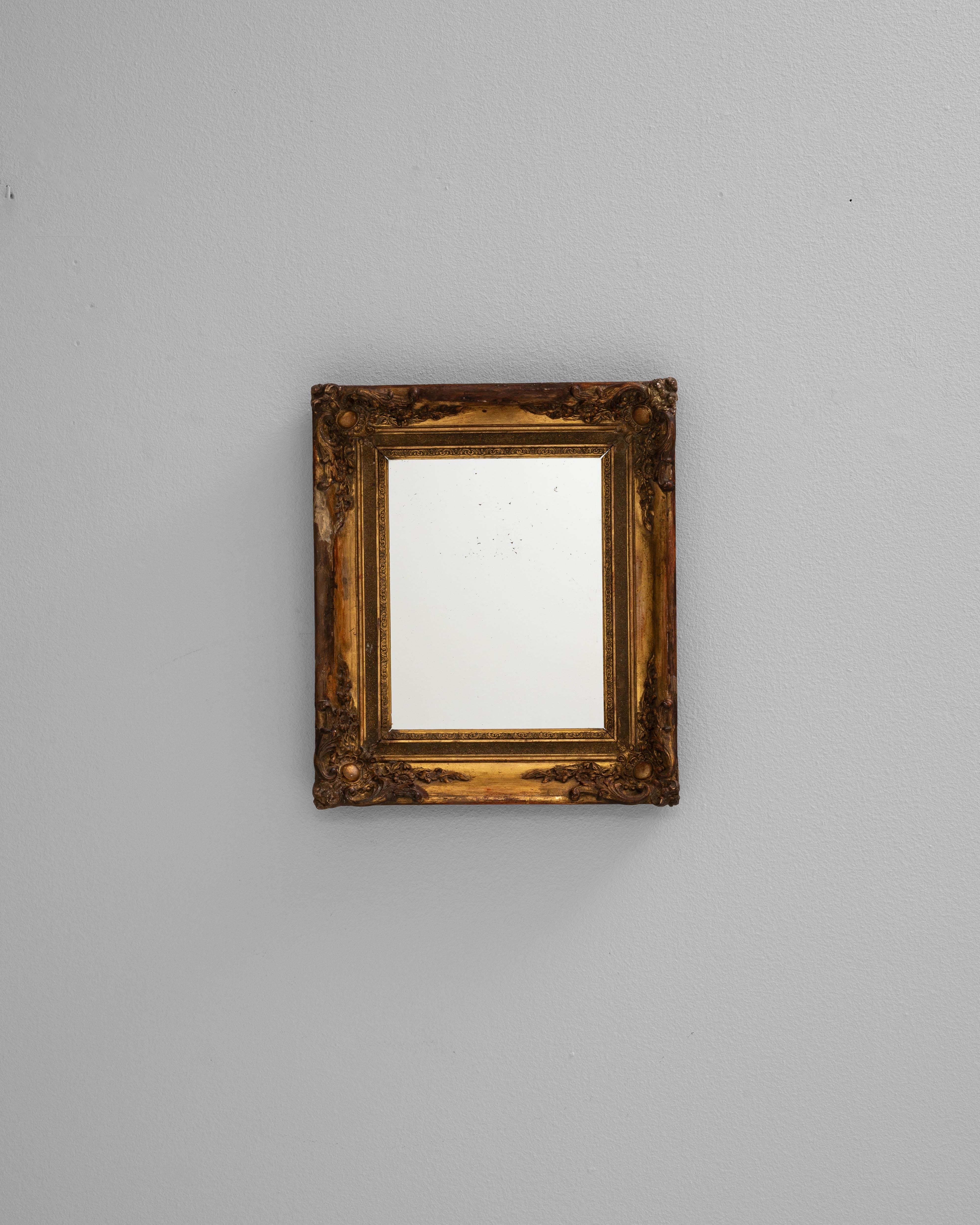 Ce miroir en bois français du XIXe siècle incarne le charme ornemental du design français classique. Le cadre en bois richement sculpté présente des motifs floraux et des volutes complexes à chaque coin, rehaussés par une finition dorée chaleureuse