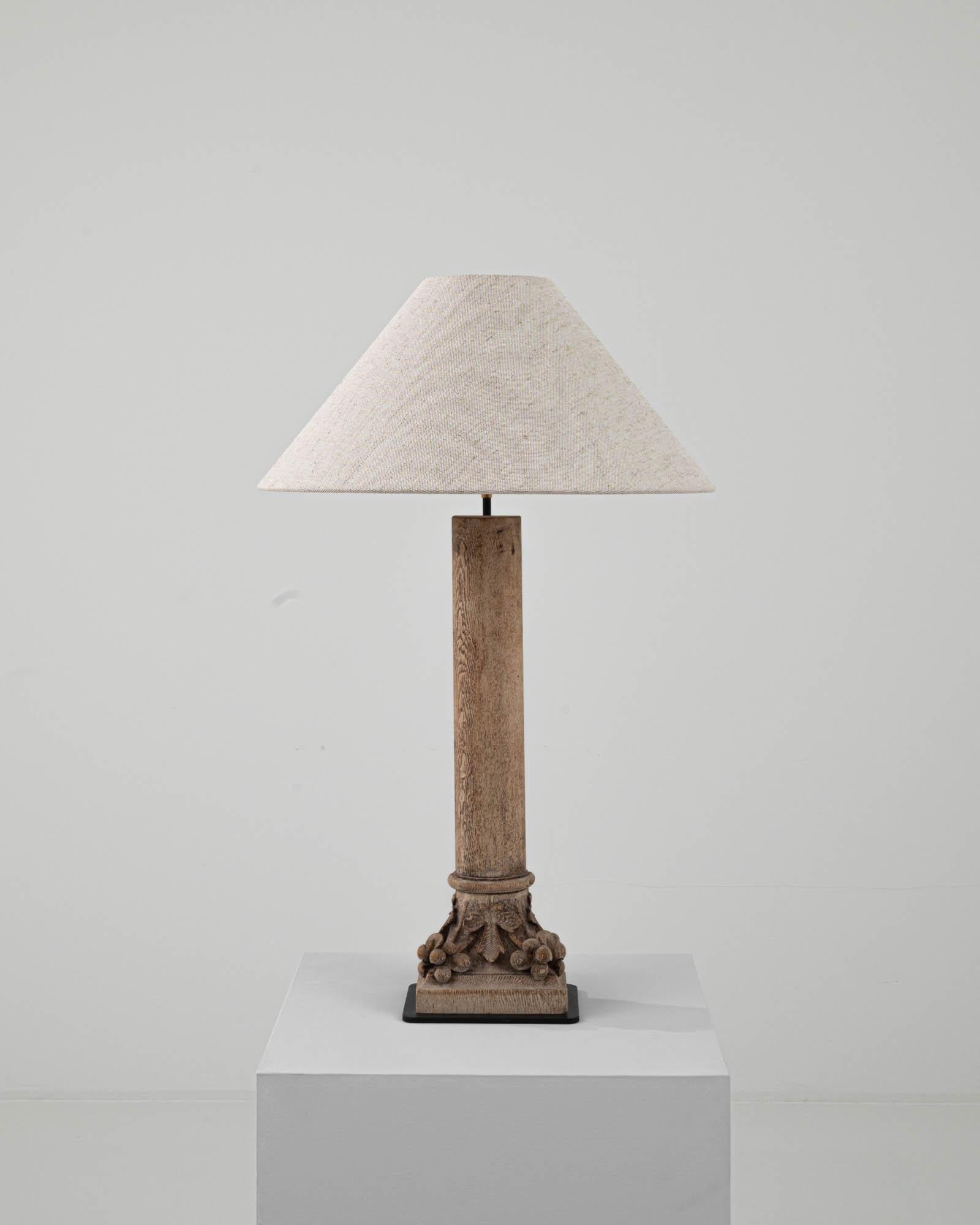 Crafted in 19th-century France, this antique lamp showcases a delicately carved wooden base adorned with exquisite foliate and bow motifs. The captivating oak wood patterns create a visually appealing and textured surface. The linen lampshade