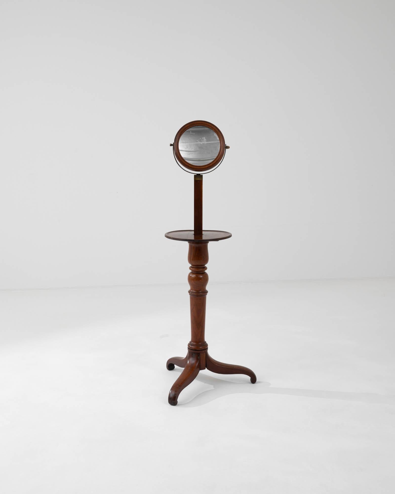 Useful both for shaving or applying makeup. The mirror can be tilted to suit many uses and is placed in an elegant round and carved frame with a brass hardware accent. This piece from nineteenth-century France, tinted to a mahogany color, comes with