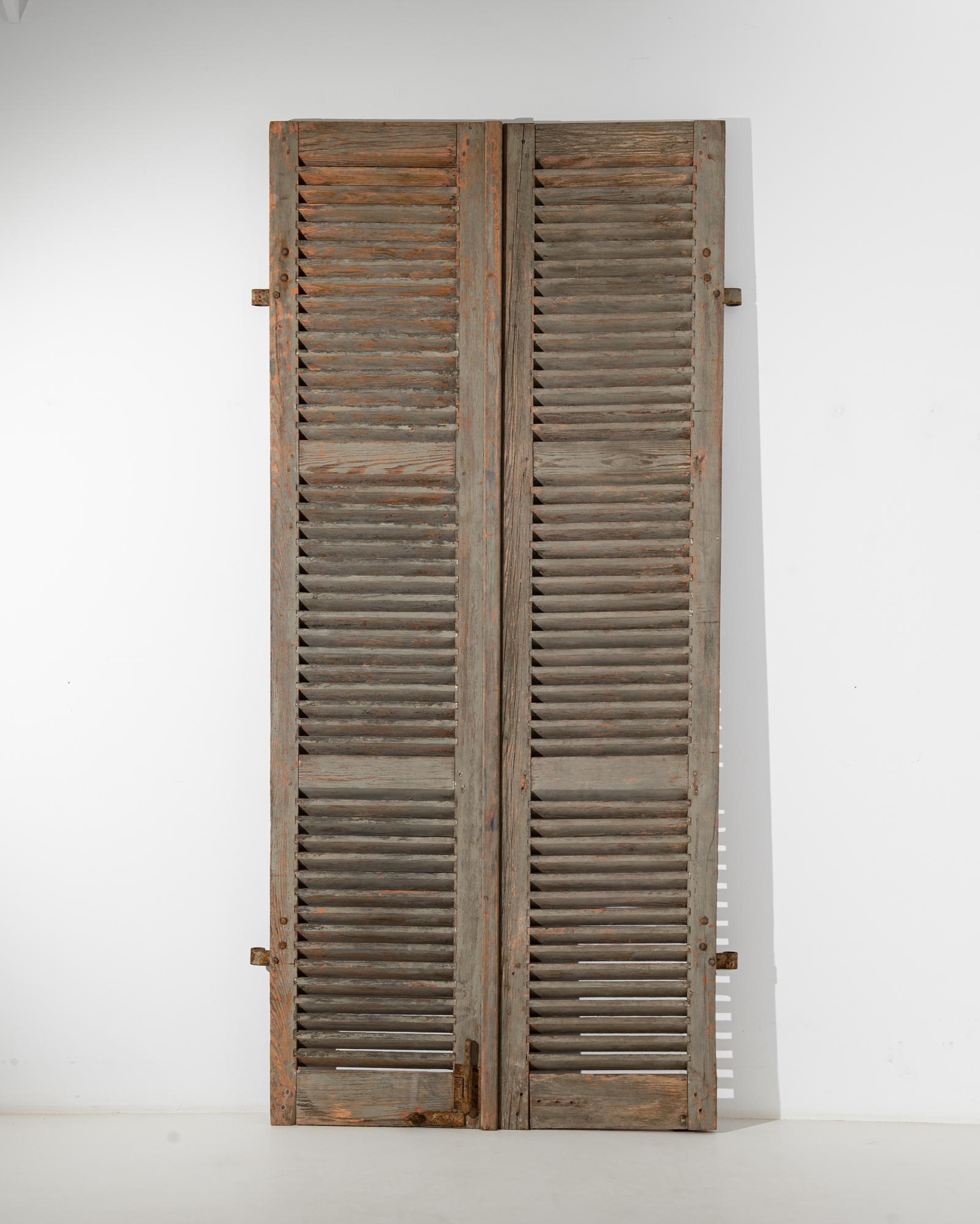 A pair of wood shutters from 19th century France. Standing at an impressive height, these vintage shutters impose their bravado while simultaneously emitting a welcoming warmth. A lively and colorful patina, a time-worn sliding bolt lock, and wooden