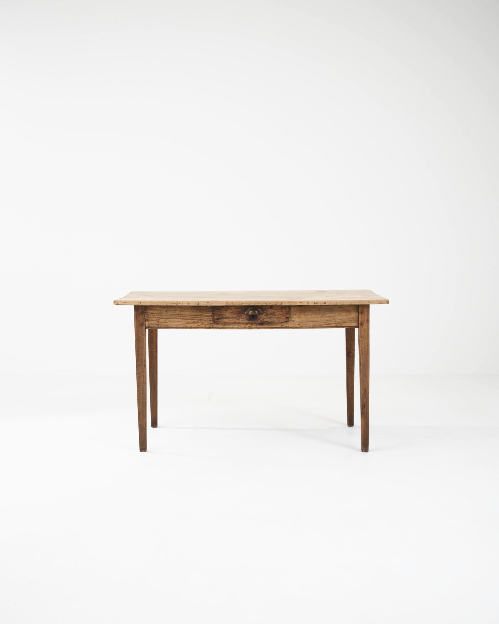 The simple design and warm finish of this antique wooden side table give it a timeless appeal. Hand-crafted in France in the 1800s, a rectangular tabletop sits atop an apron housing a small drawer, perfect for odds and ends. The subtle taper of the