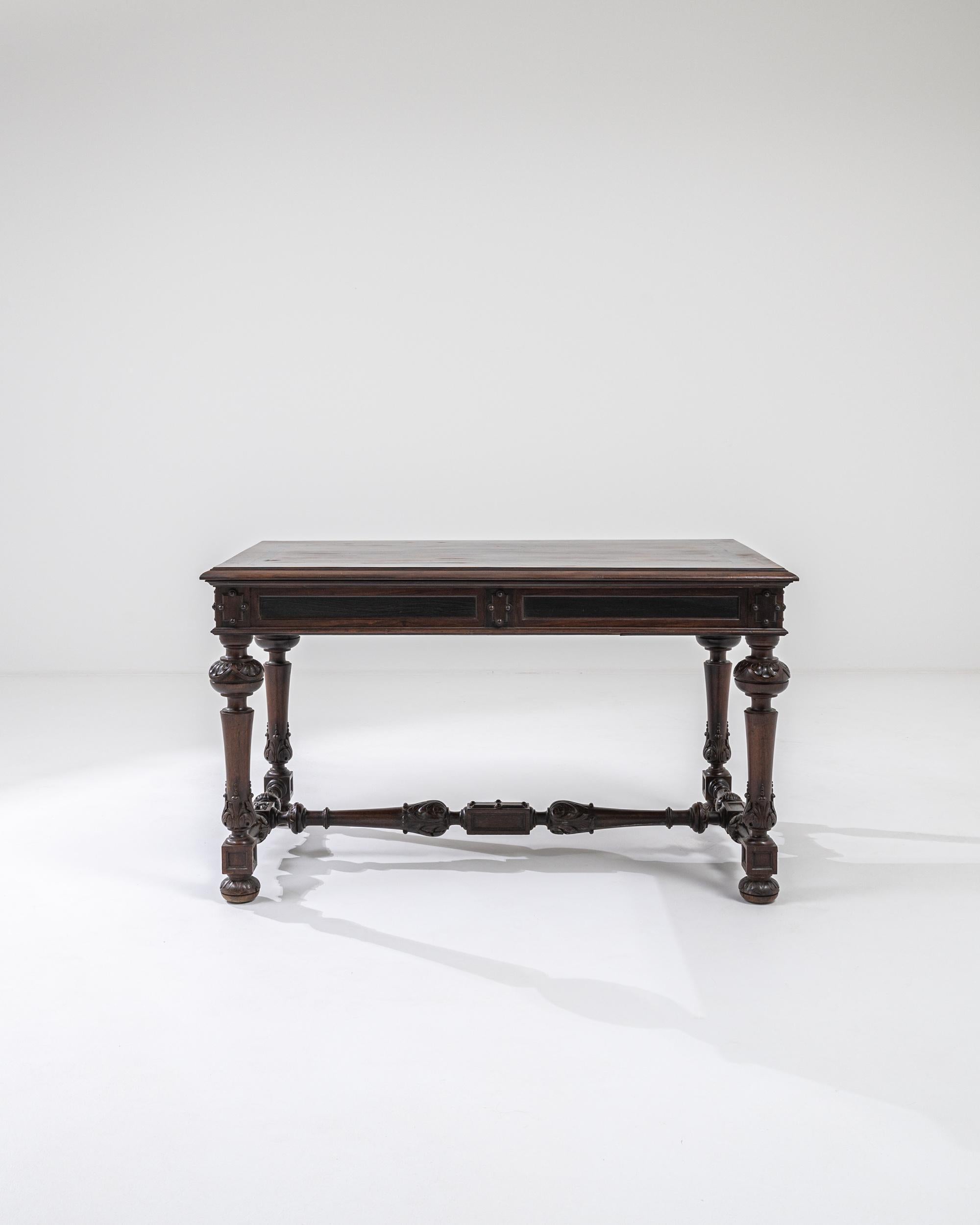 A wooden table from 19th century France. Sumptuously hand-carved details line this table’s aprons and shape the contours of its legs, creating a dazzling display of fastidious craftsmanship. Two sliding drawers extend from either end of the table,