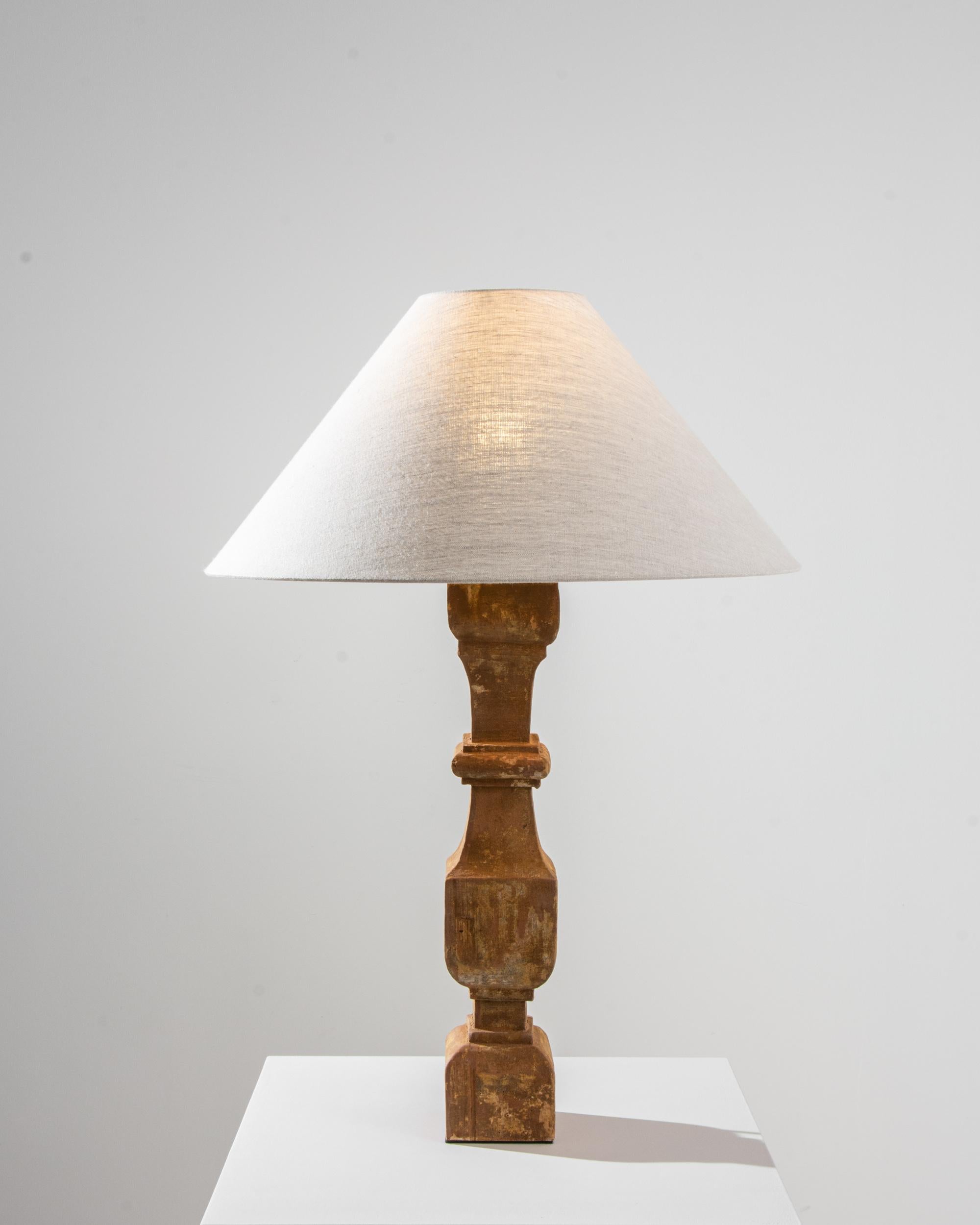 The harmonious simplicity and warm patina of this wooden table lamp make a delightful antique accent. The base is made from a repurposed Provincial table leg, built in France in the 1800s. Bead-and cove details and stretcher blocks bring a pleasing