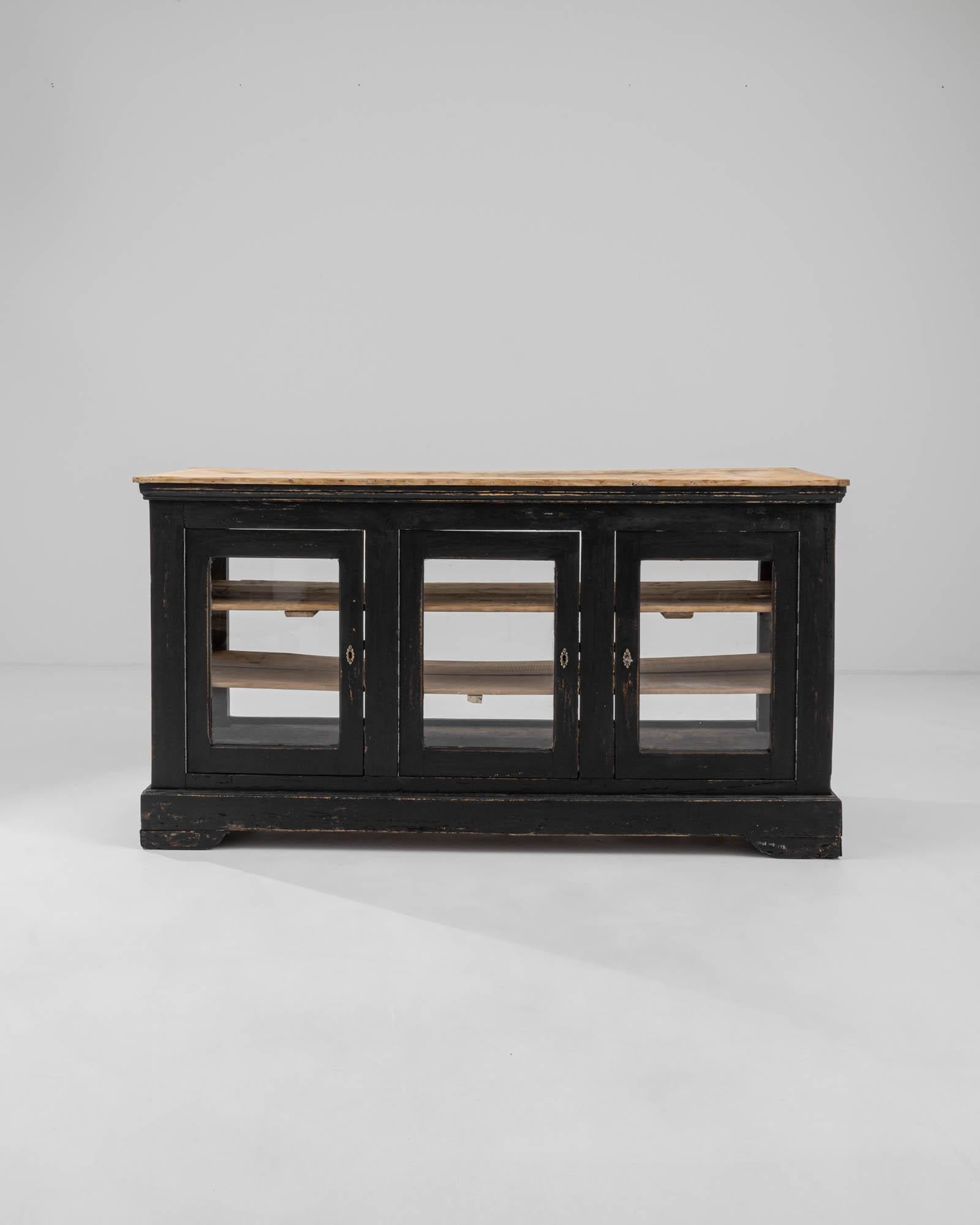 Supported by a sturdy ogee bracket base, this 19th-century French wooden bar features three glass panel doors that provide a view into its spacious interior. Additionally, the cabinet offers three small drawers at the back. Two lengthy shelves