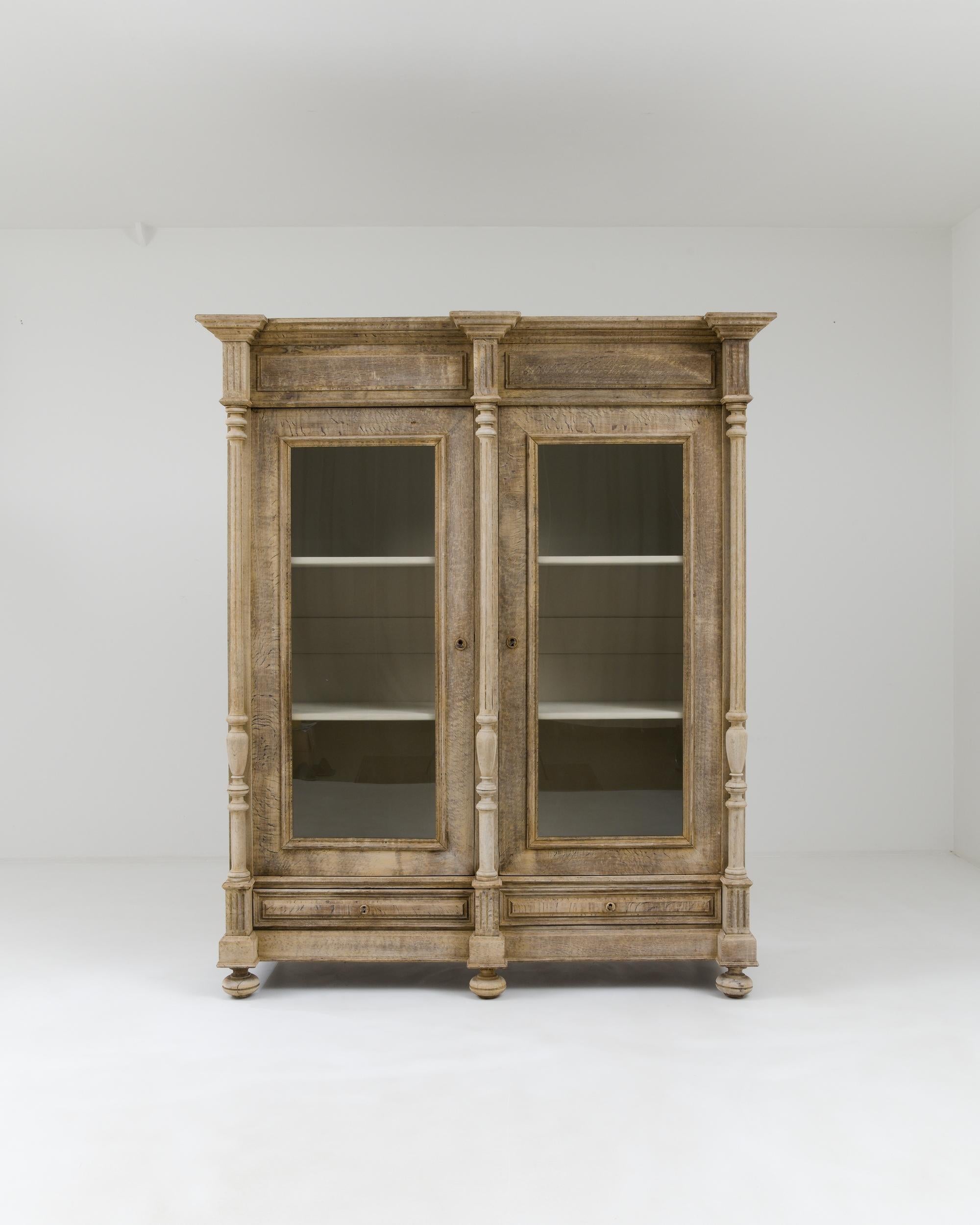 A wooden vitrine created in 19th century, France. A grand demonstration of elite craftsmanship and classical beauty, this enormous vitrine towers overhead with a regal aura. The patinated oak has been carefully restored with a bleached finish,