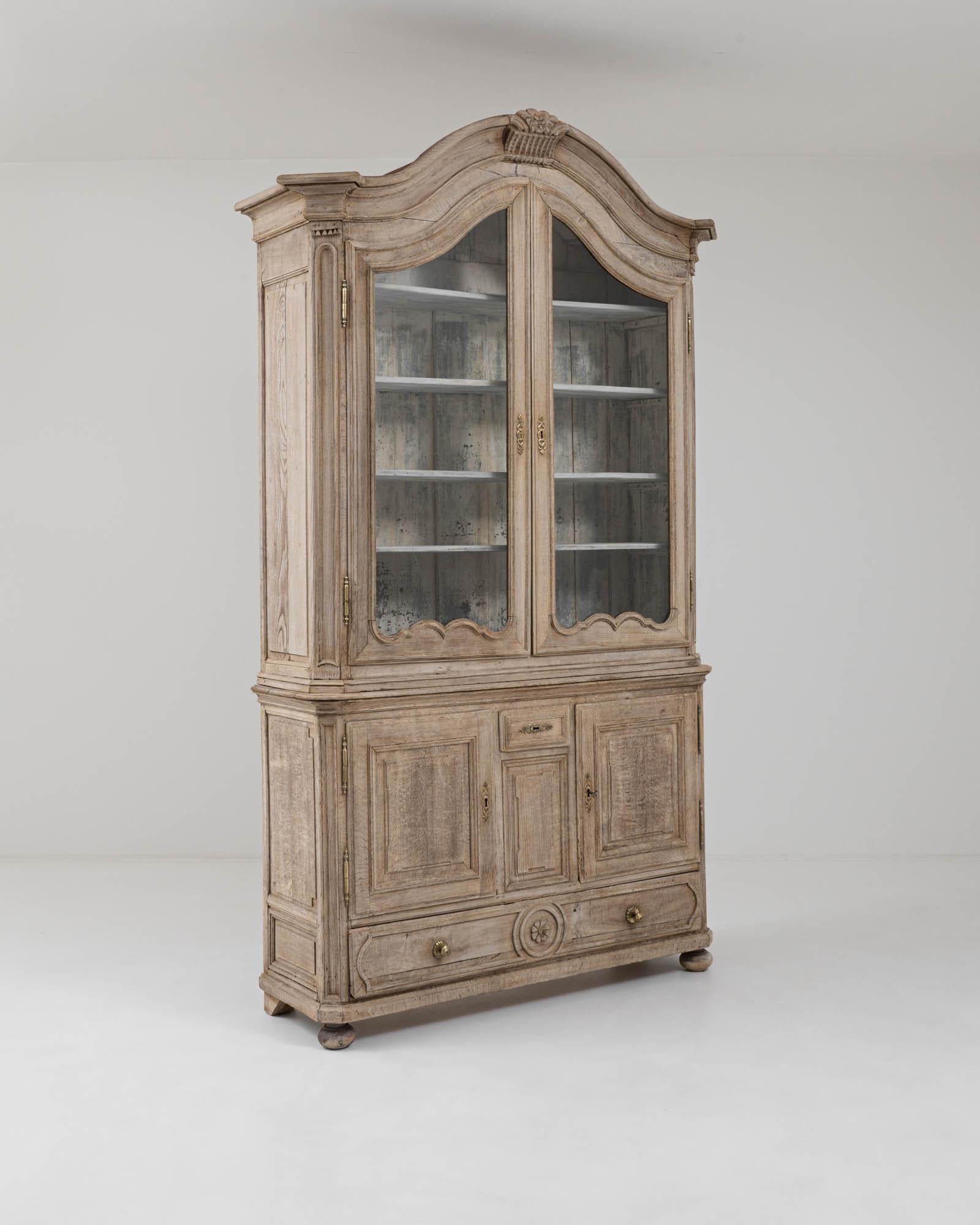 A wooden vitrine created in 19th century France. Standing with a classical poise, this vitrine towers overhead, beckoning one toward it with its French Provincial elegance. Emphatically carved floral and scroll motifs and handsome brass hardware