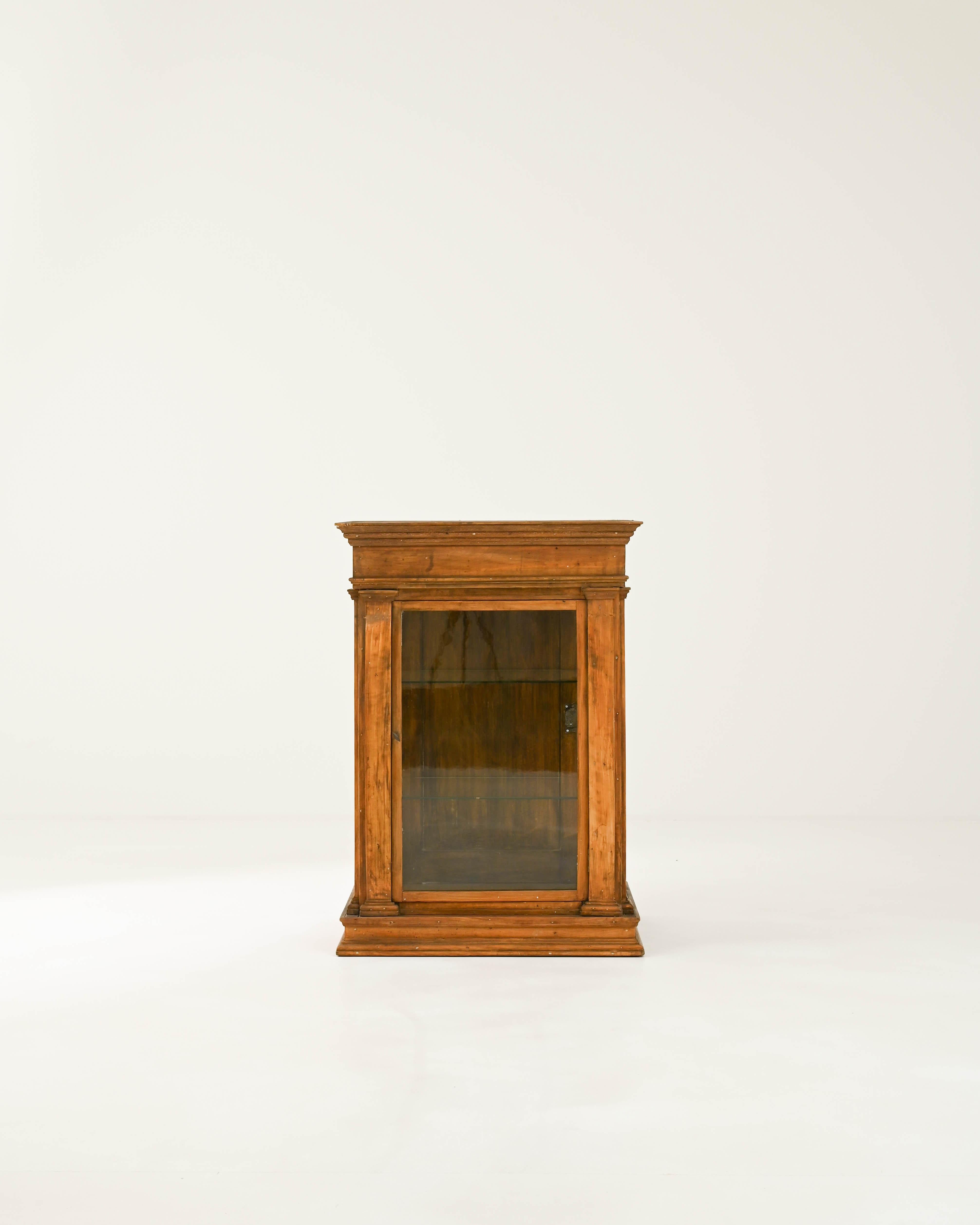 The dignified design and warm patina of this antique wooden vitrine give it a timeless appeal. Hand-built in France in the 1800s, the form has a Neoclassical character: the carved pilasters that frame the windows of the case and the elegant upper
