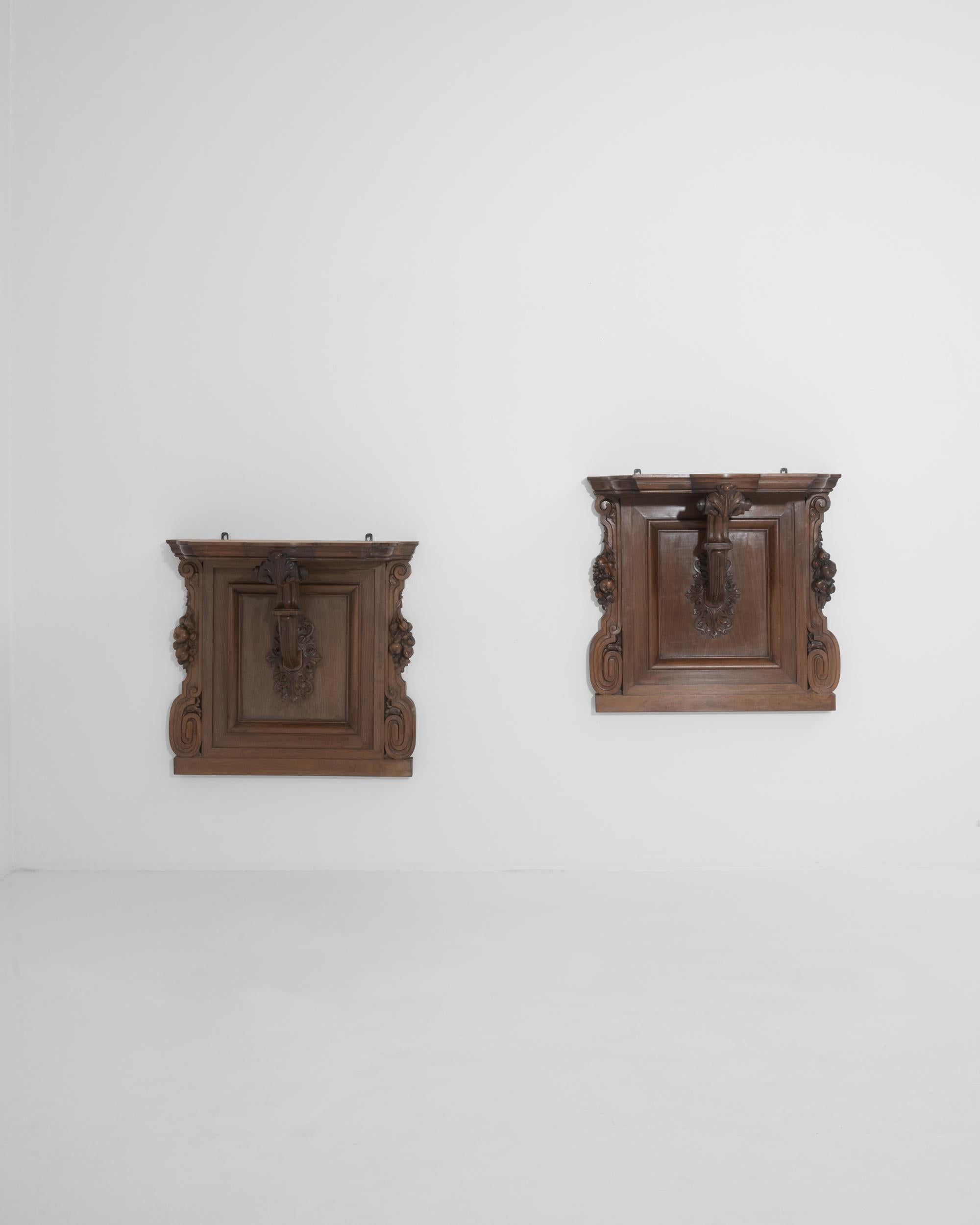 A pair of wooden wall consoles made during the 19th century in France. A stylized corbel extends from the center of each console to support the wall mounted shelf. A chocolate brown hue colors this pair, the moody warmth creating a versatile mood to